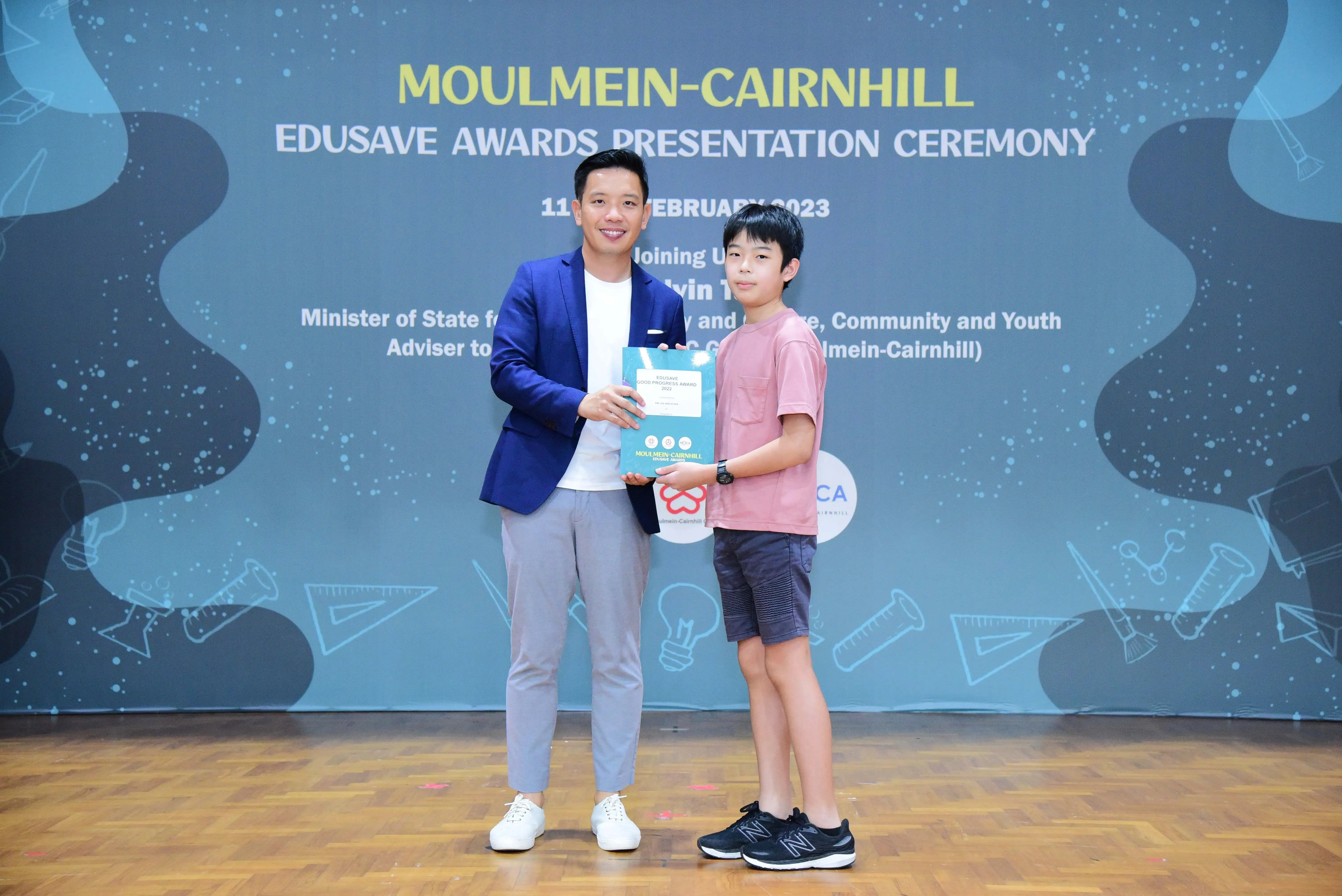 An adult and a young boy hold an award certificate at the Moulmein-Cairnhill Edusave Awards Presentation Ceremony 2023.