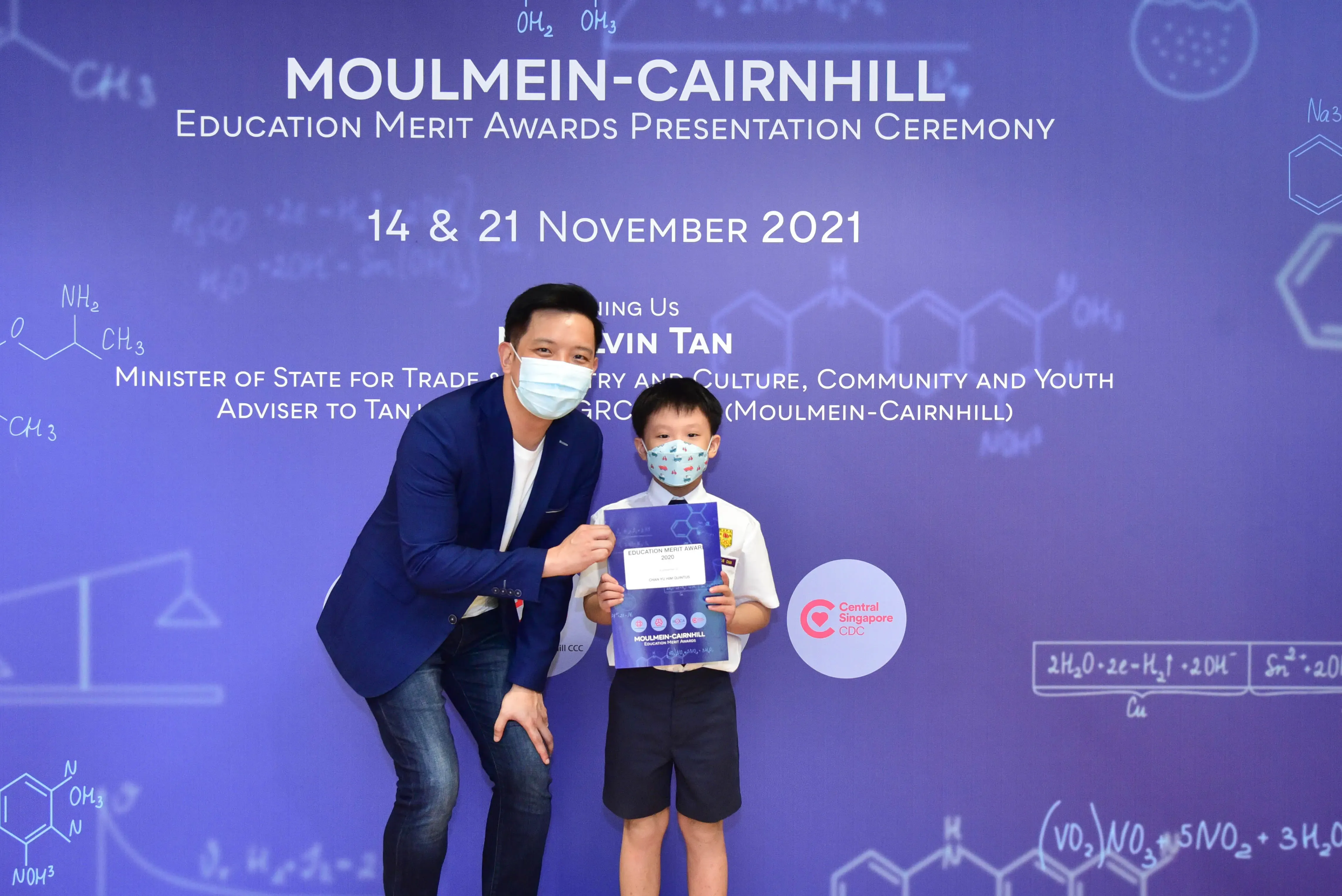 A masked man and young boy hold a certificate at the Moulmein-Cairnhill Education Merit Awards Ceremony, November 2021.