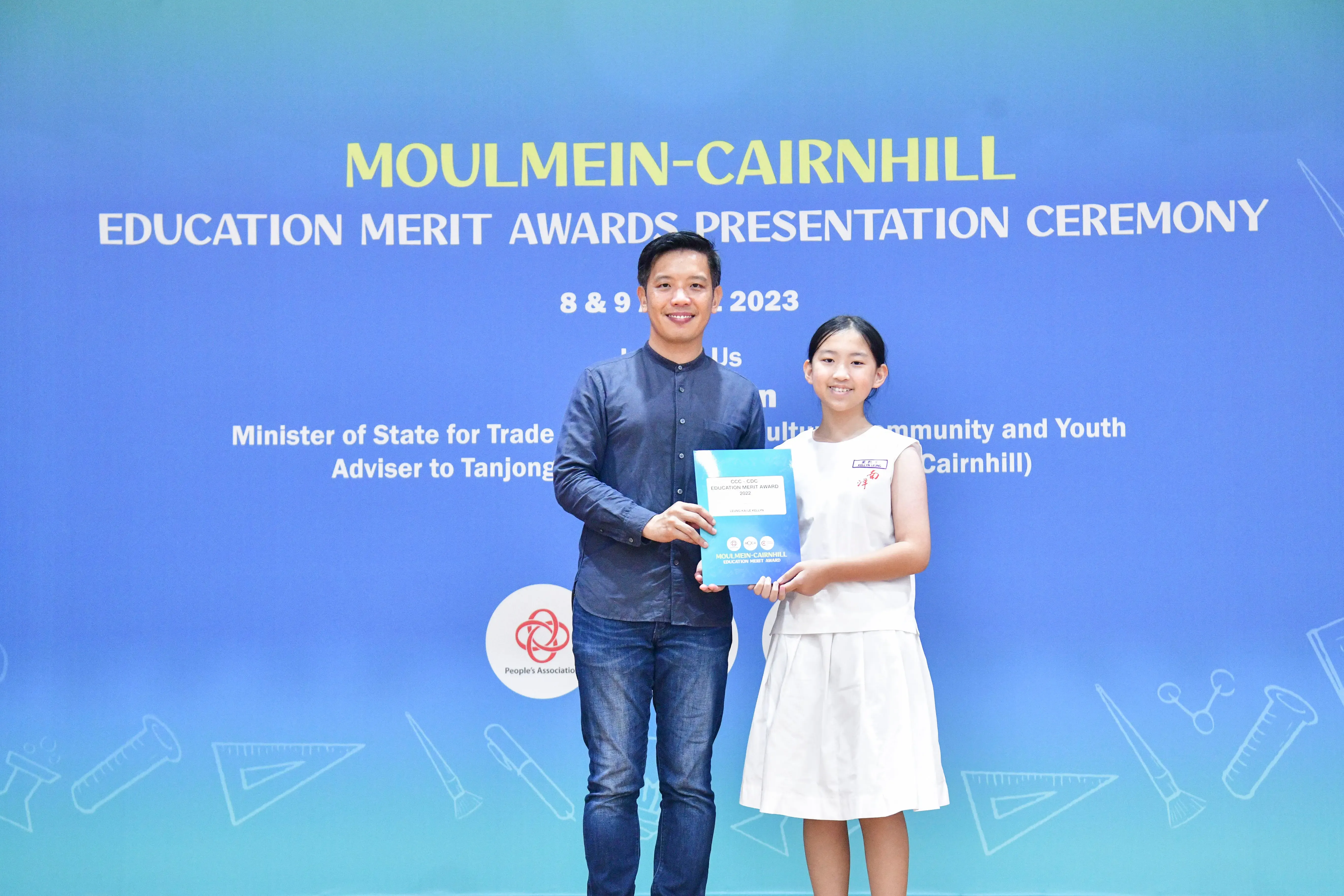 A man and a young girl hold an award certificate at the Moulmein-Cairnhill Education Merit Awards Ceremony 2023.