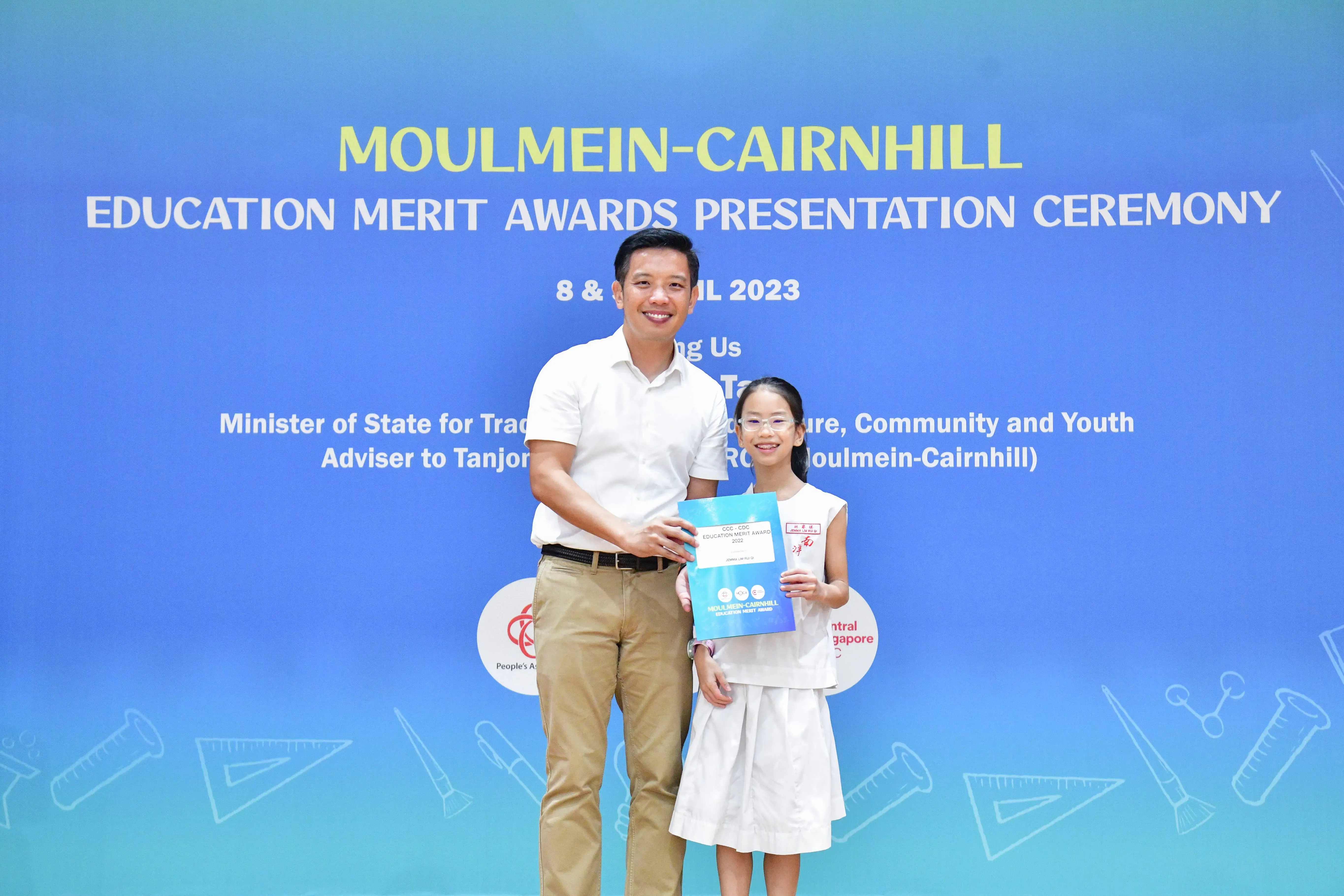 A man and a young girl hold an award certificate at the Moulmein-Cairnhill Education Merit Awards Ceremony 2023.
