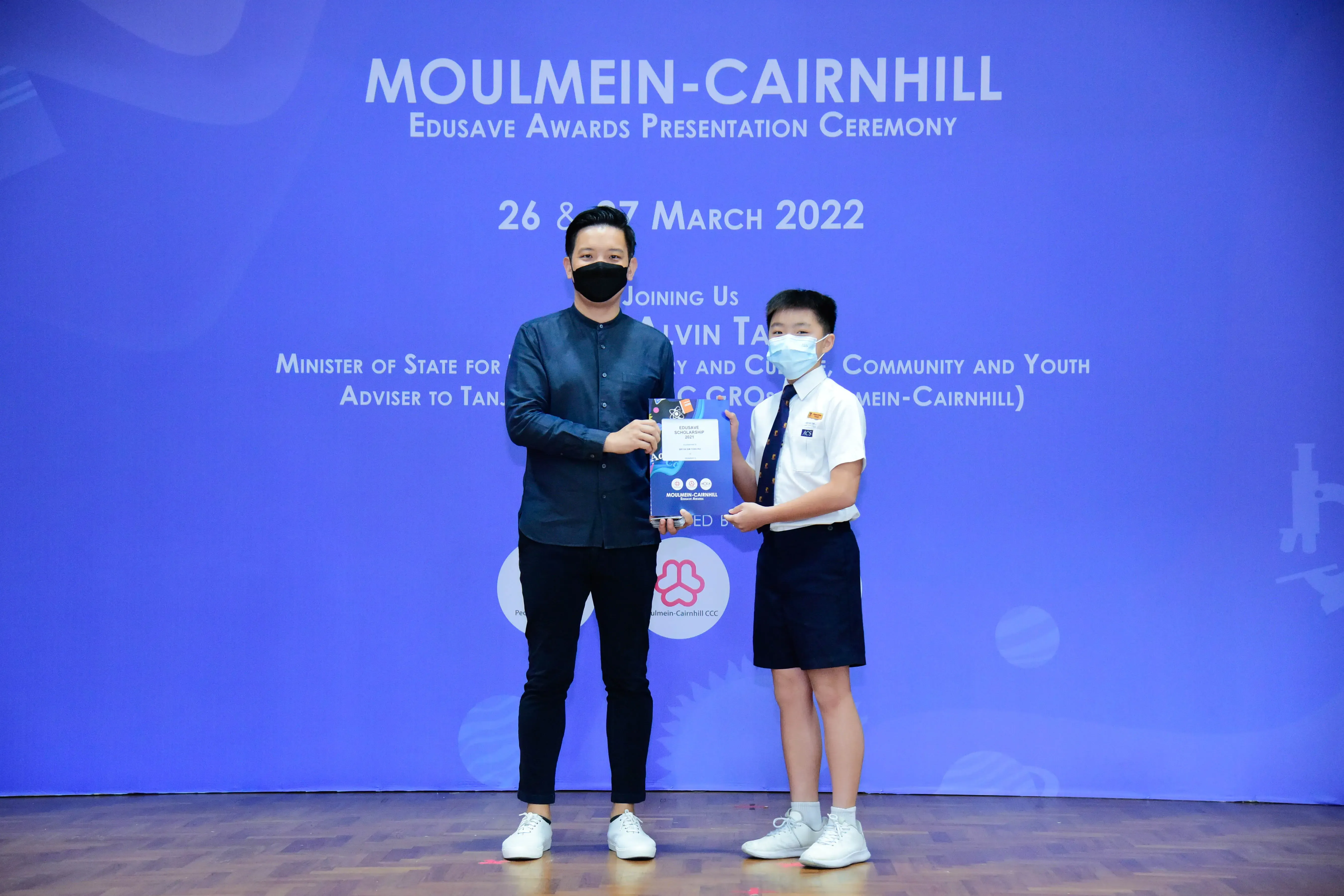 An adult and a uniformed student hold an award at the Moulmein-Cairnhill Edusave Awards Ceremony, March 2022.