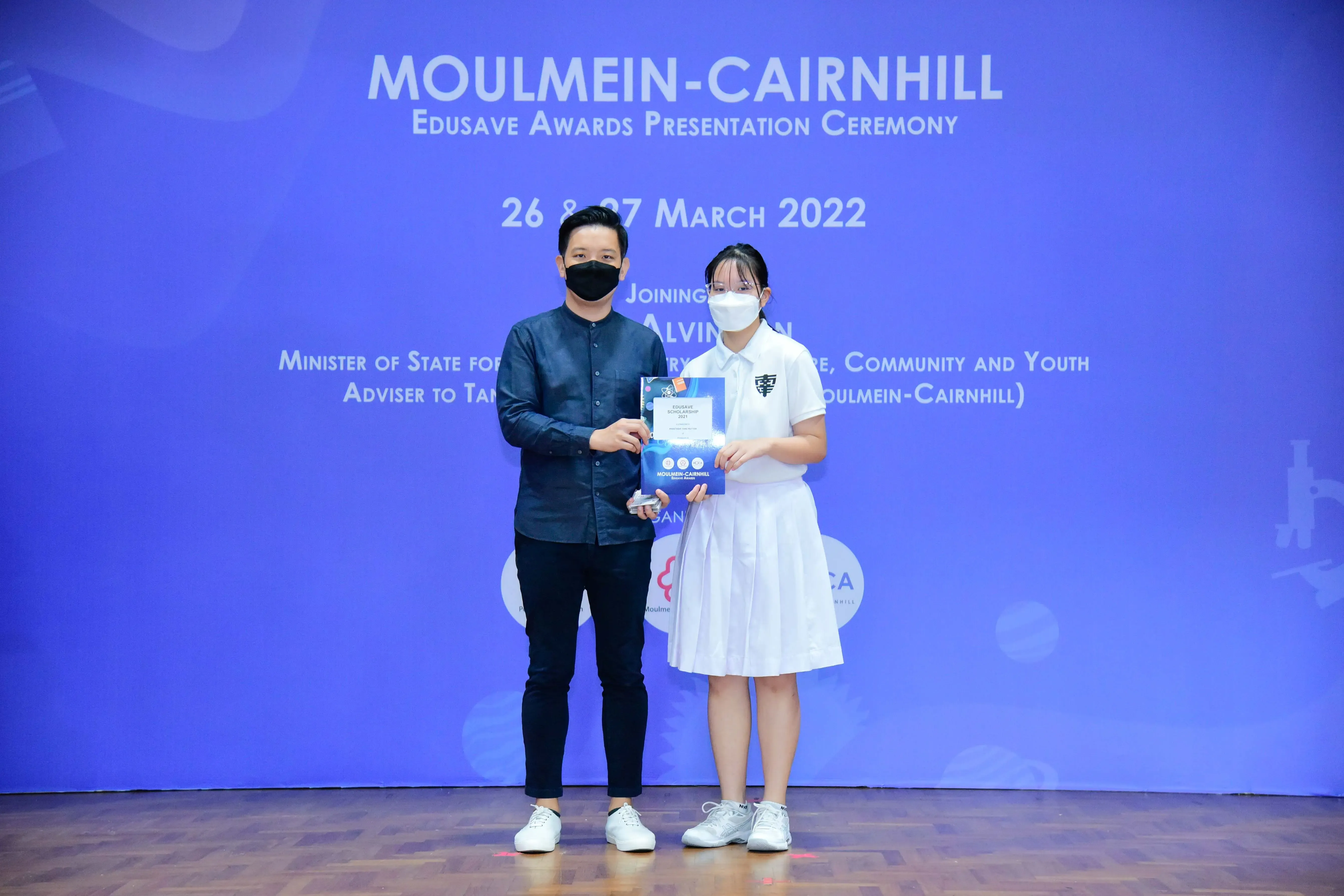 Two masked individuals hold an award certificate at the Moulmein-Cairnhill Edusave Awards Presentation Ceremony, March 2022.