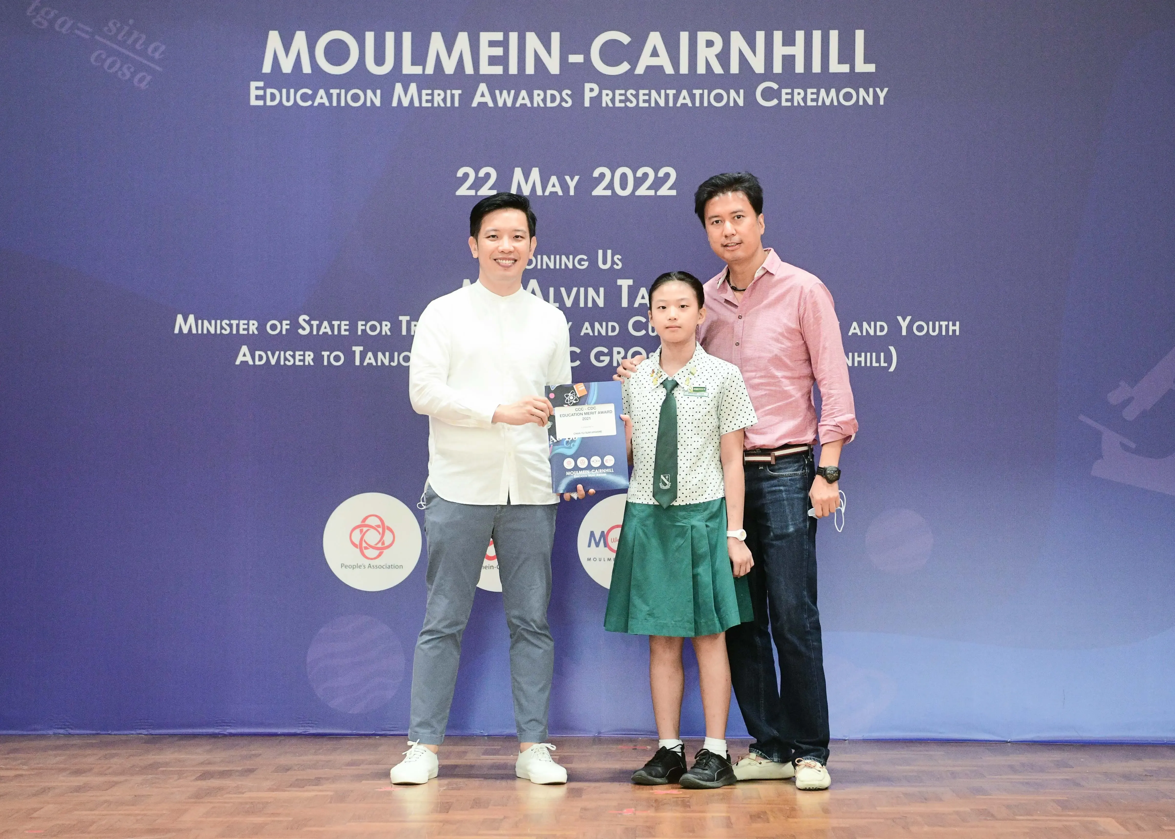 Three people pose at the Moulmein-Cairnhill Education Merit Awards ceremony on 22 May 2022, with a student holding an award.