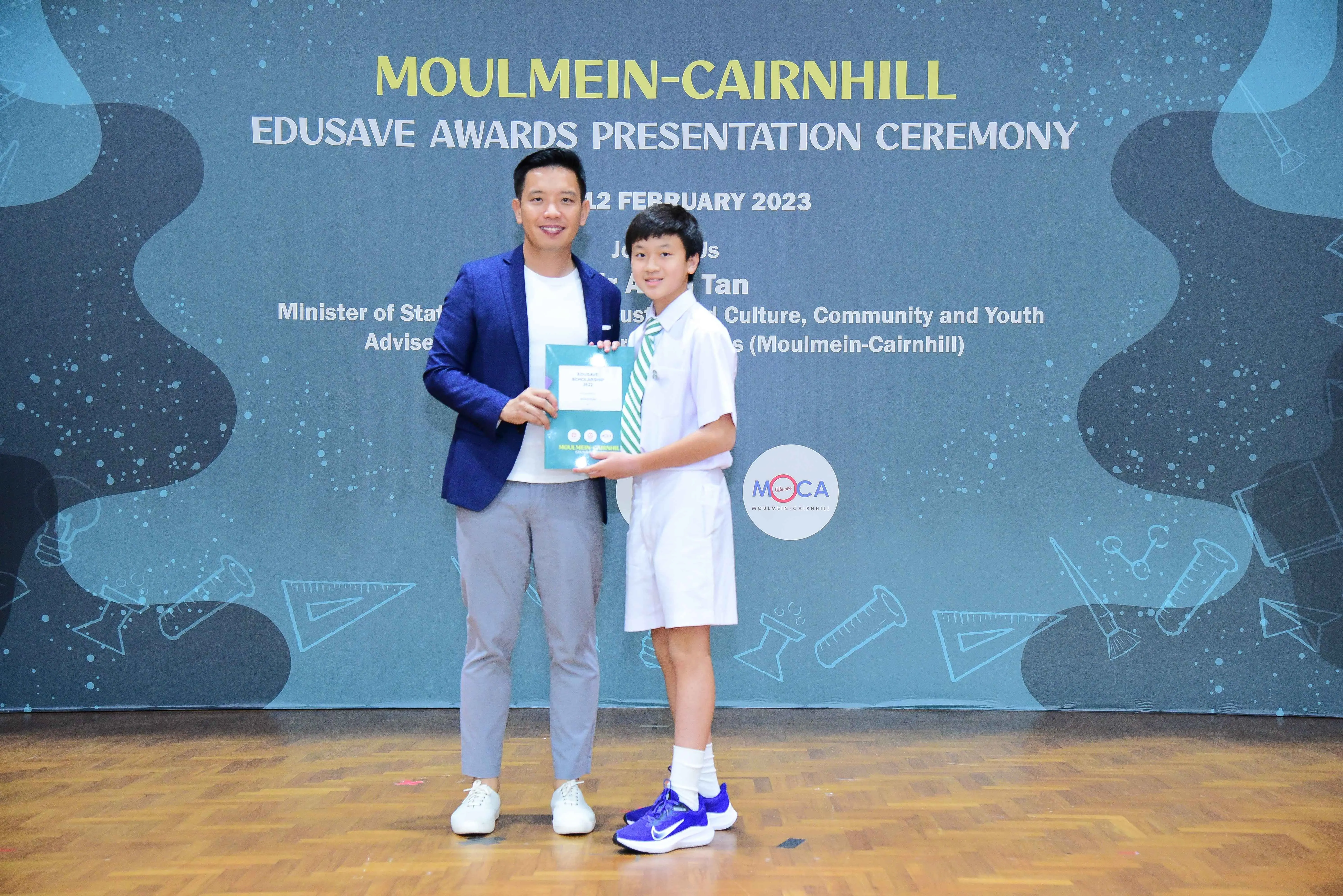 A man in a blue blazer and a young boy in school uniform hold an award at the Moulmein-Cairnhill Edusave Awards 2023.