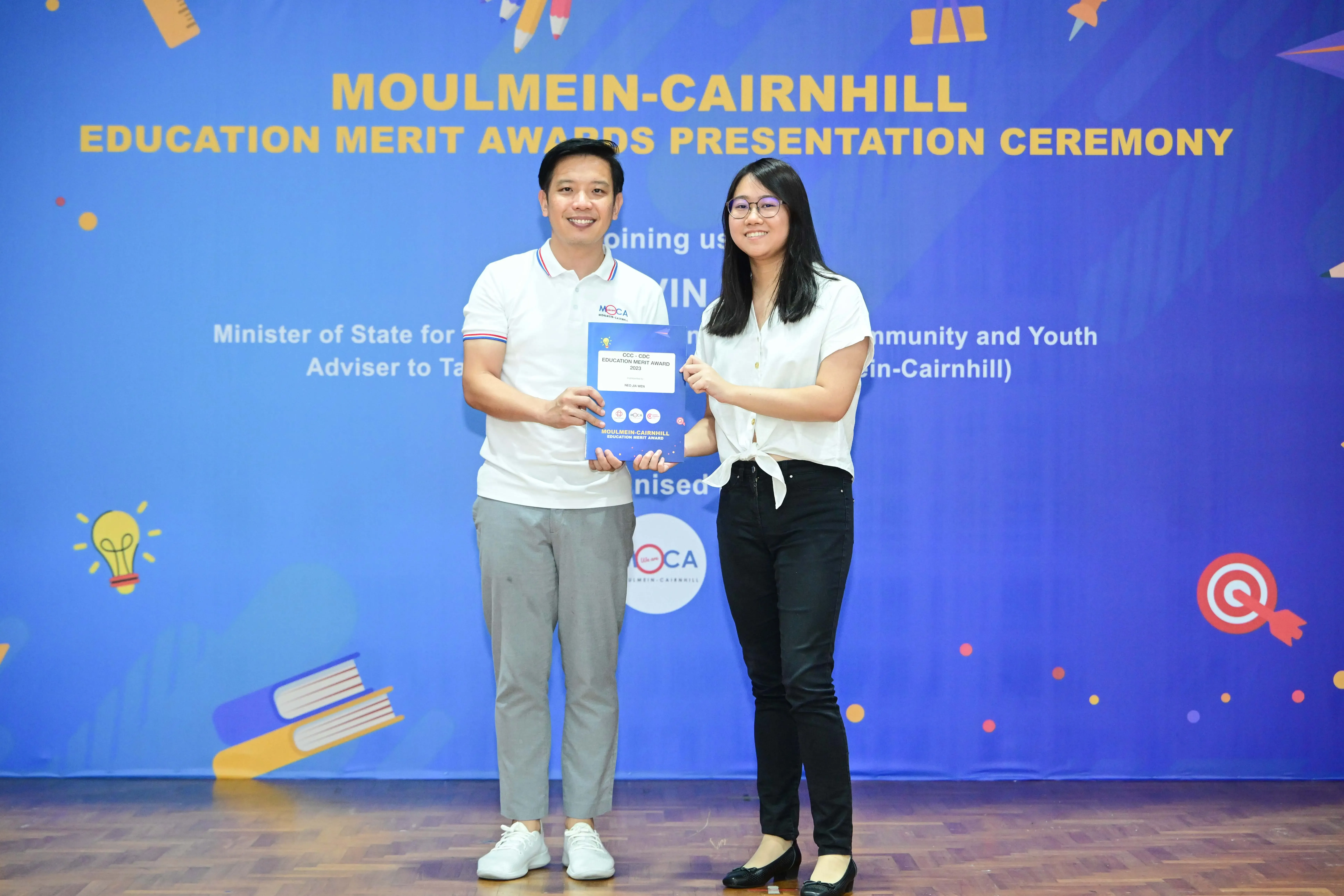 Two people smile while holding a certificate at the Moulmein-Cairnhill Education Merit Awards Presentation Ceremony.