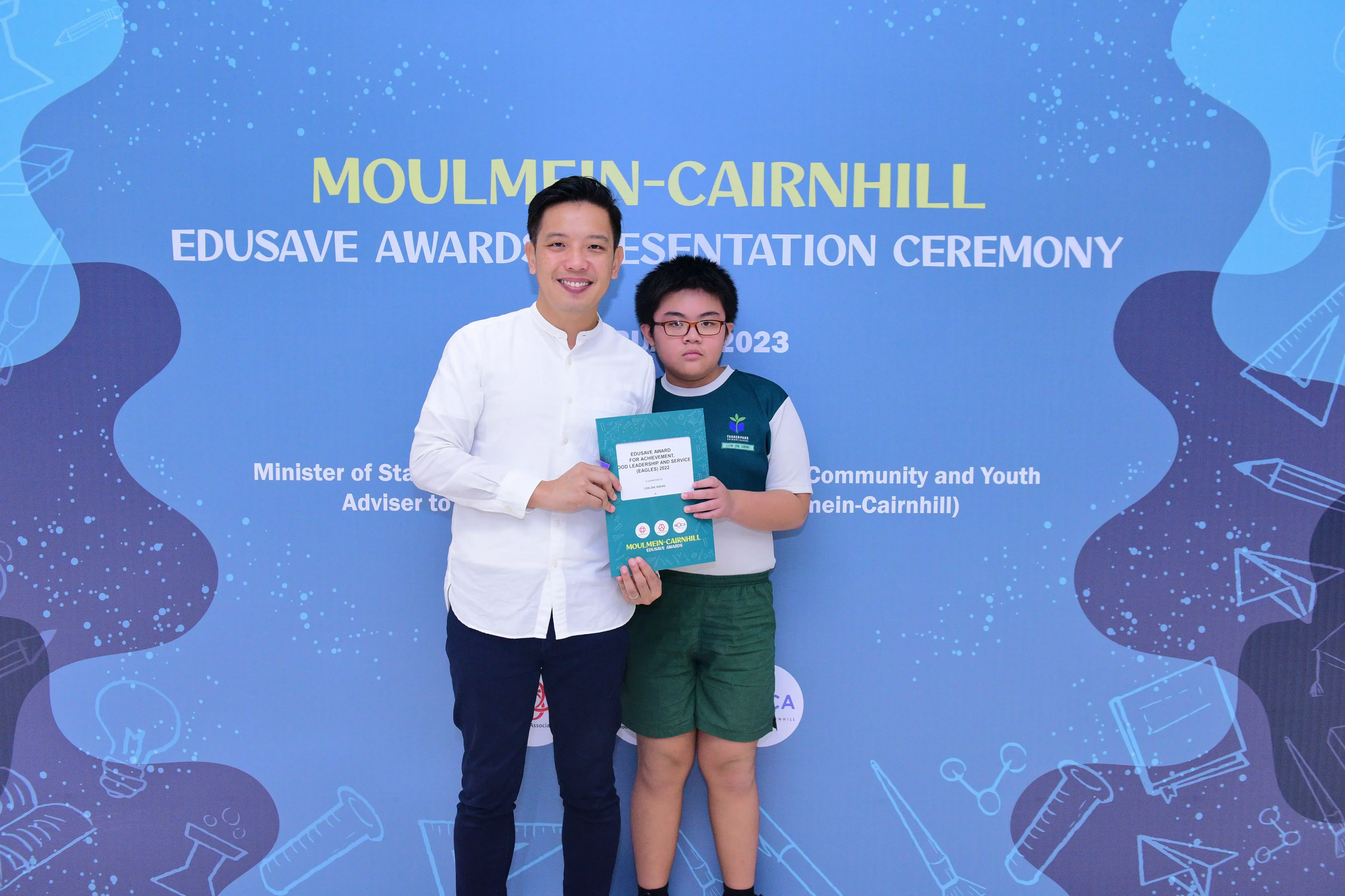An adult and a young student hold an award certificate at the Moulmein-Cairnhill Edusave Awards Presentation Ceremony 2023.