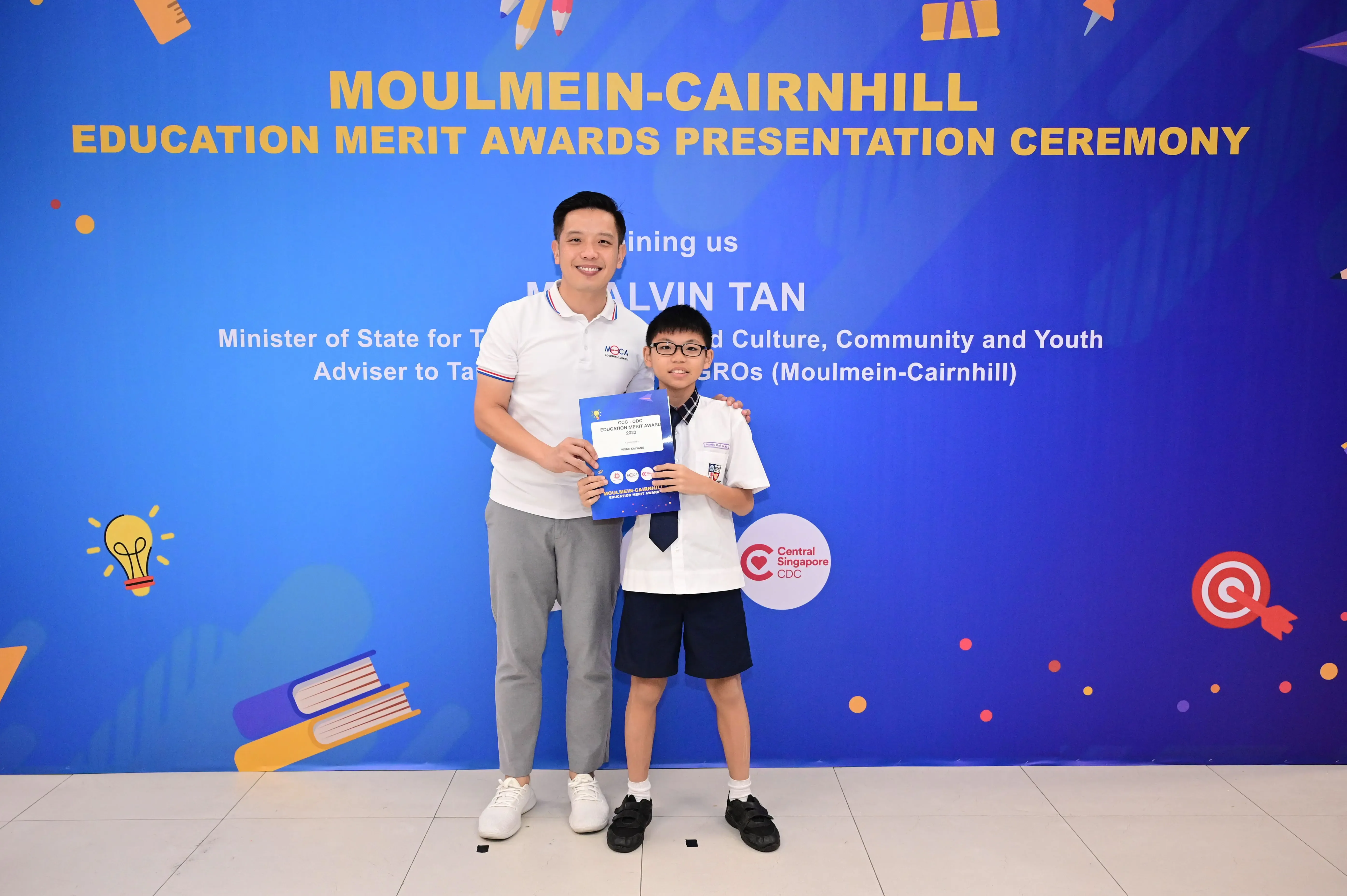 A man and a young student in school uniform hold a certificate at the Moulmein-Cairnhill Education Merit Awards ceremony.