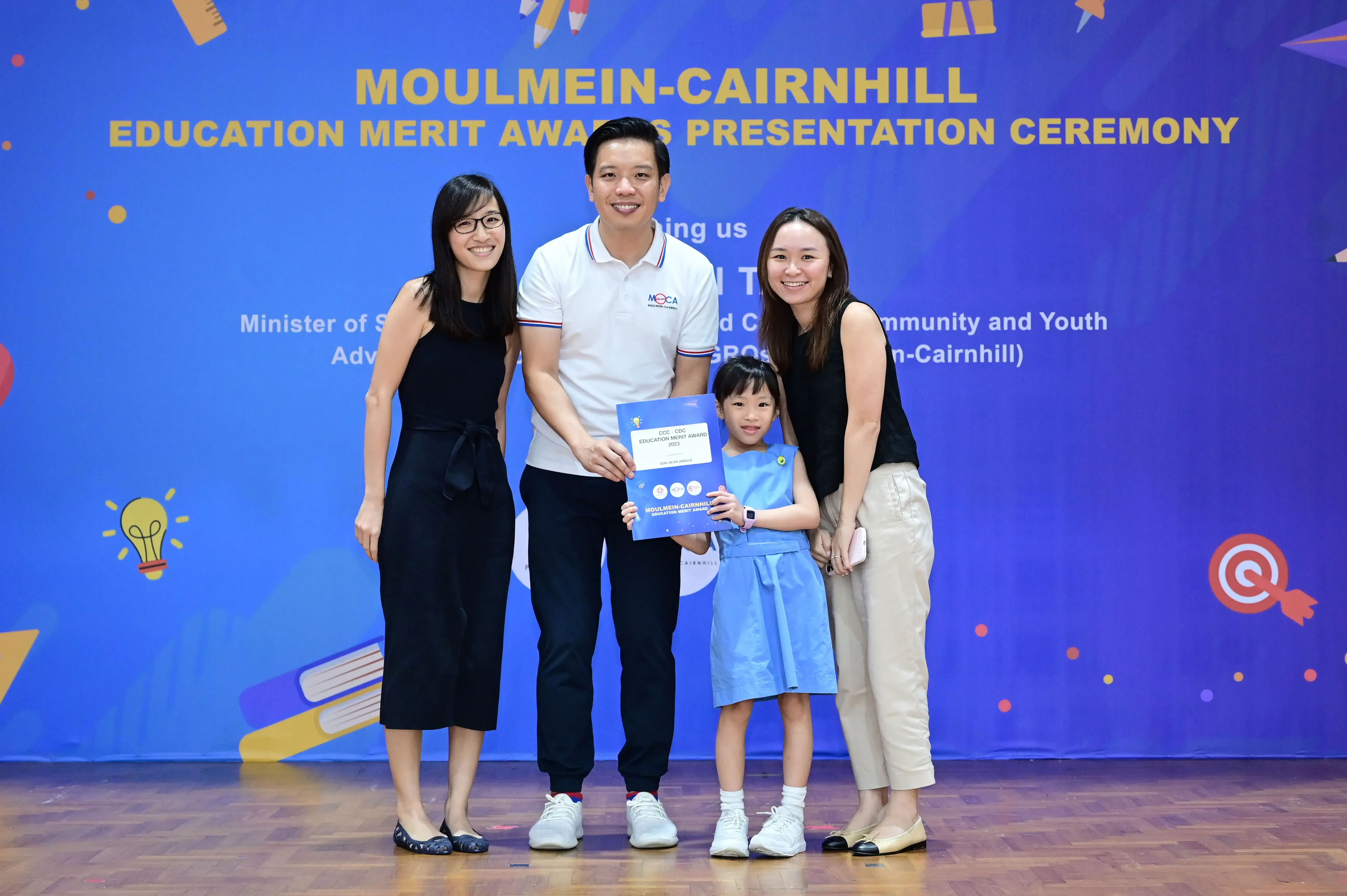 Three adults and a young girl pose with an award certificate at the Moulmein-Cairnhill Education Merit Awards ceremony.