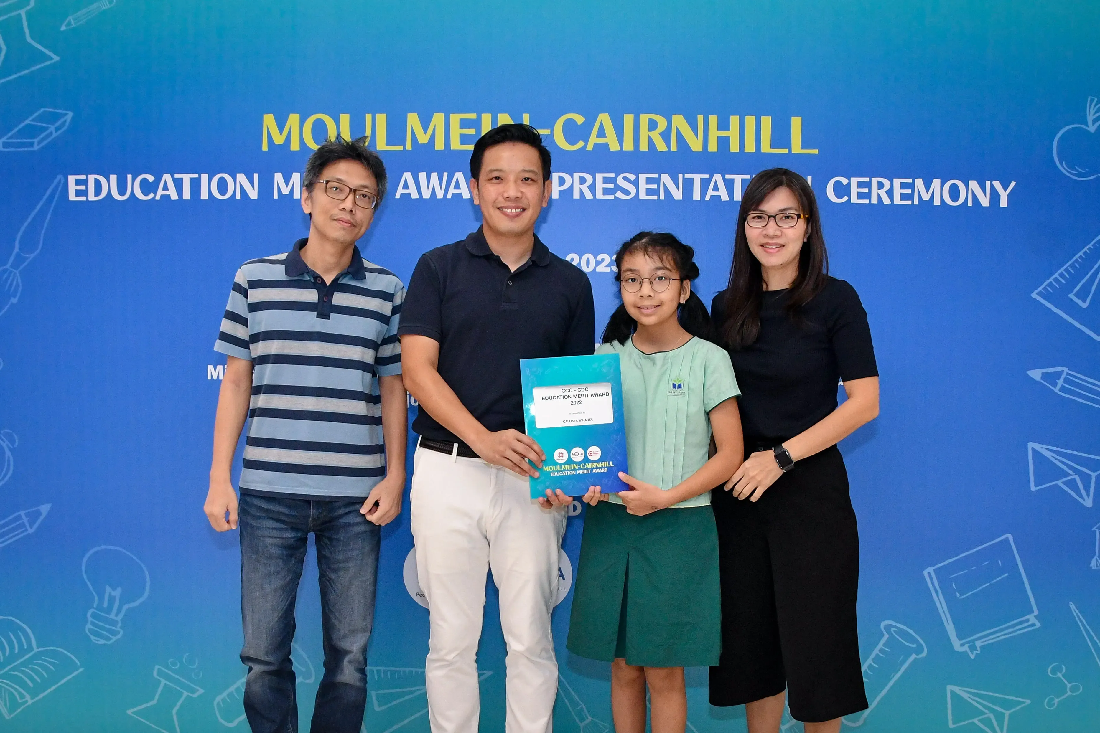 Three adults and a young girl pose holding an award certificate at the Moulmein-Cairnhill Education Merit Award Ceremony.