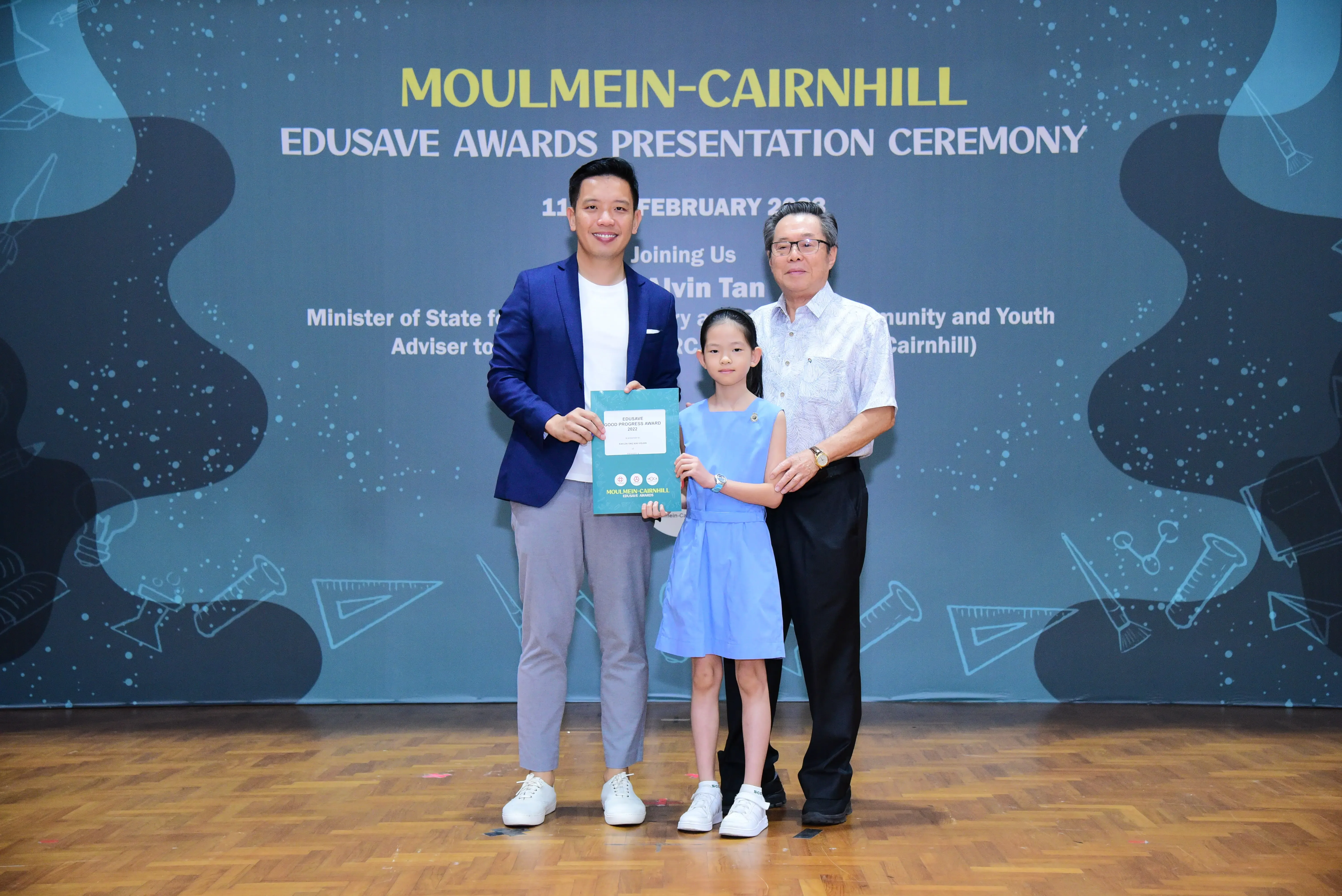 Two men and a young girl hold a certificate at the Moulmein-Cairnhill Edusave Awards Presentation Ceremony.