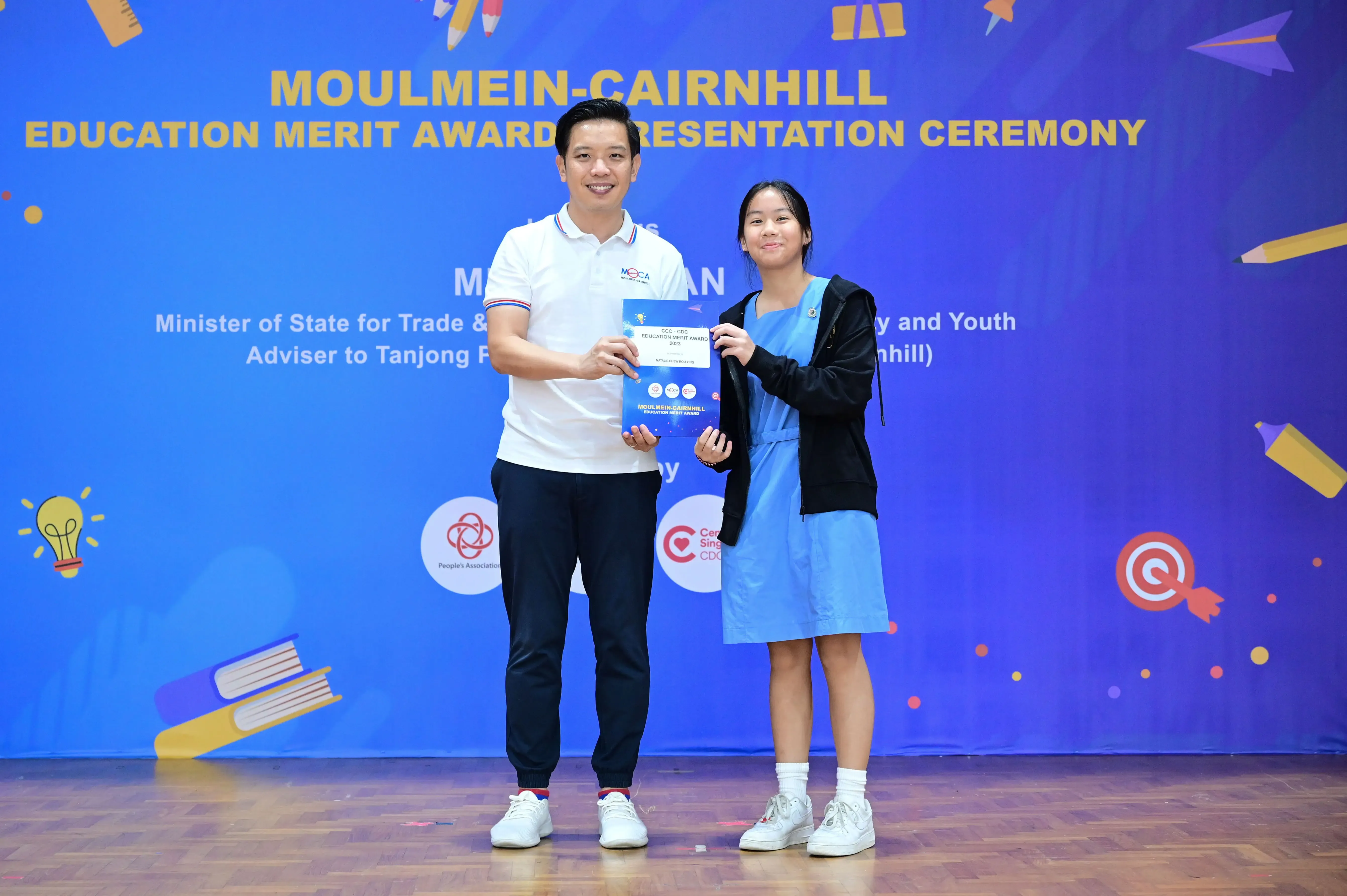 Man and young girl hold a certificate together at Moulmein-Cairnhill Education Merit Award Presentation Ceremony.