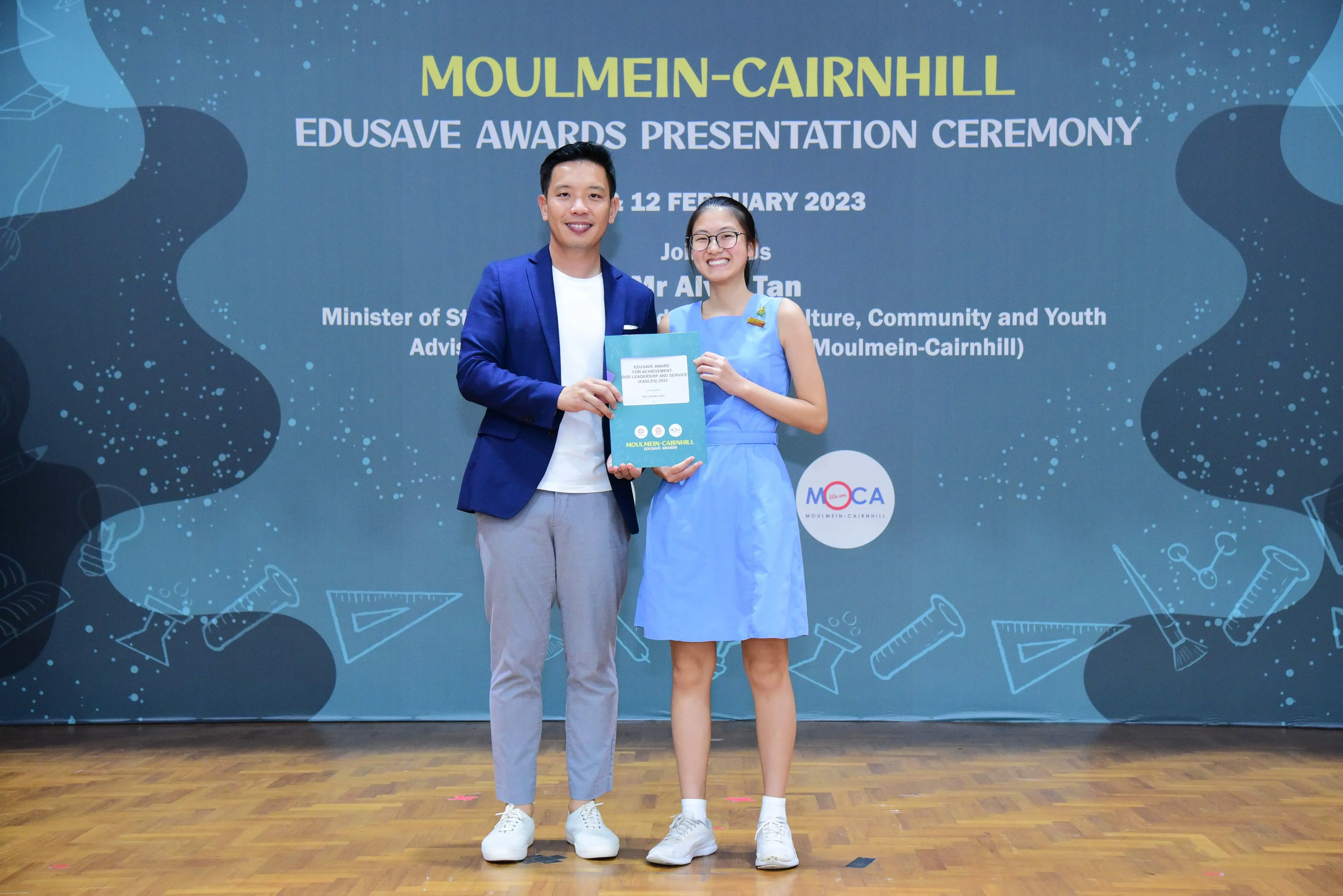 Two people smile holding an award certificate at the Moulmein-Cairnhill Edusave Awards Presentation Ceremony, February 2023.