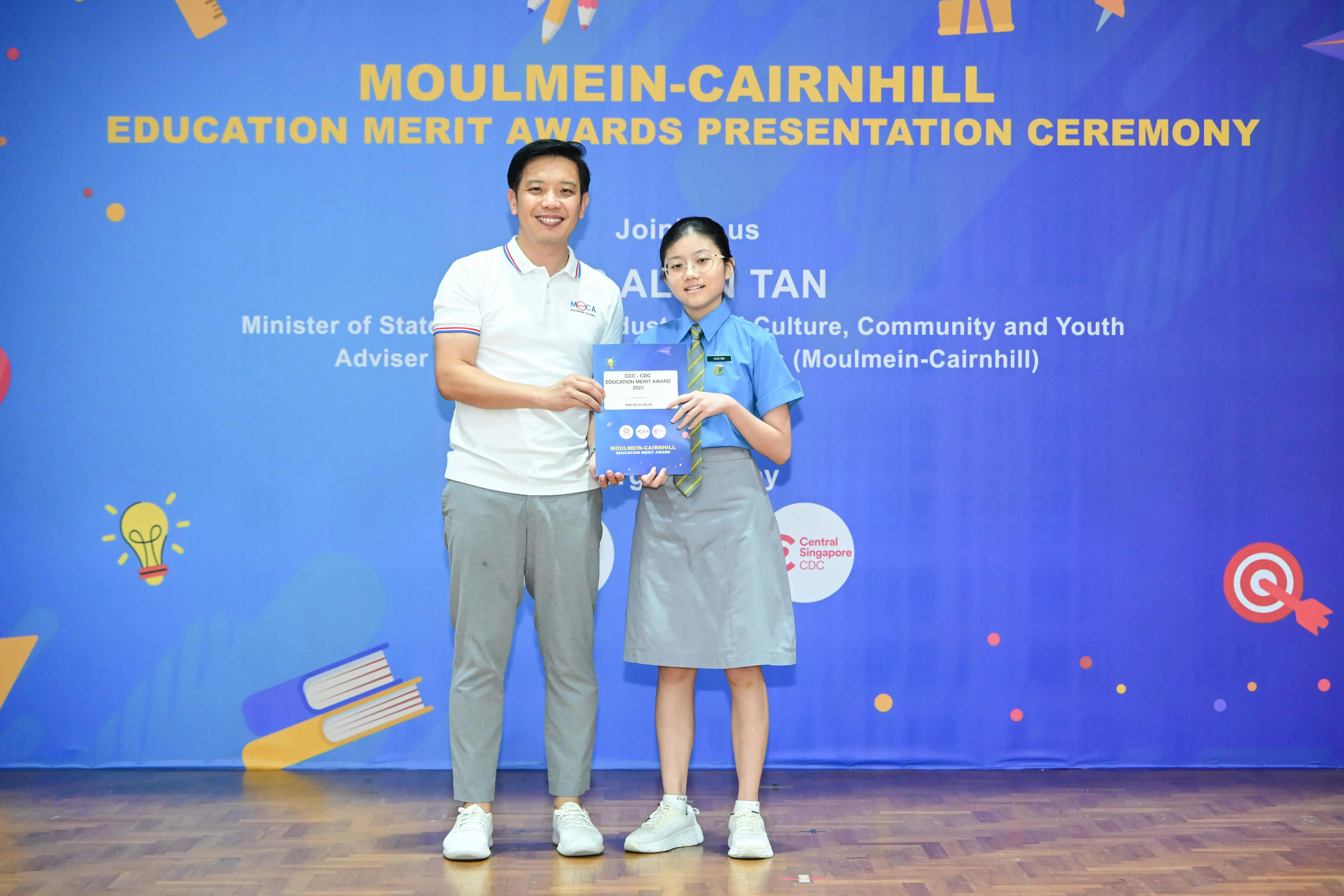 A man and a young student in school uniform hold a certificate at the Moulmein-Cairnhill Education Merit Awards ceremony.