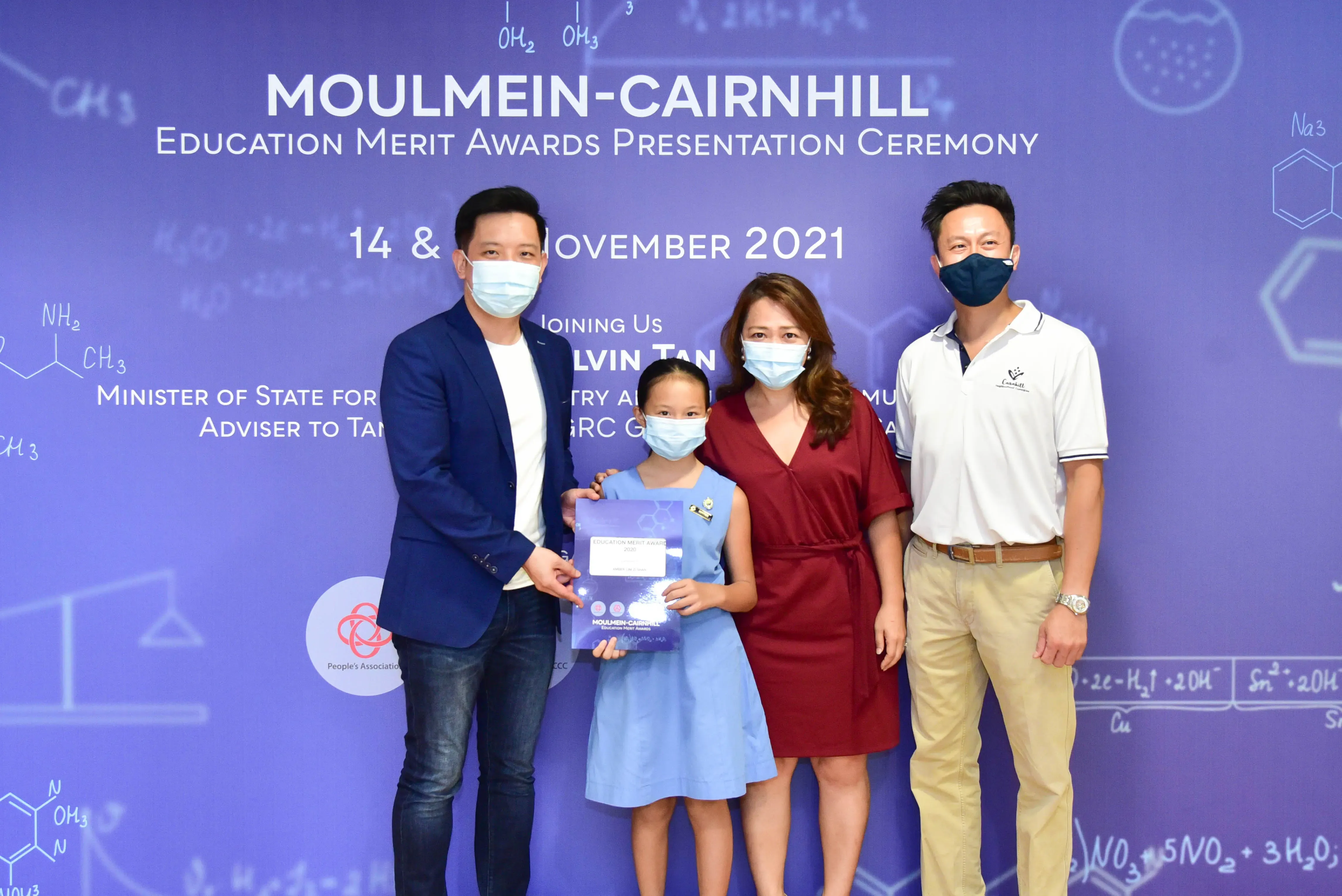 Four masked people pose at the Moulmein-Cairnhill Education Merit Awards Ceremony in November 2021, with a girl holding an award.