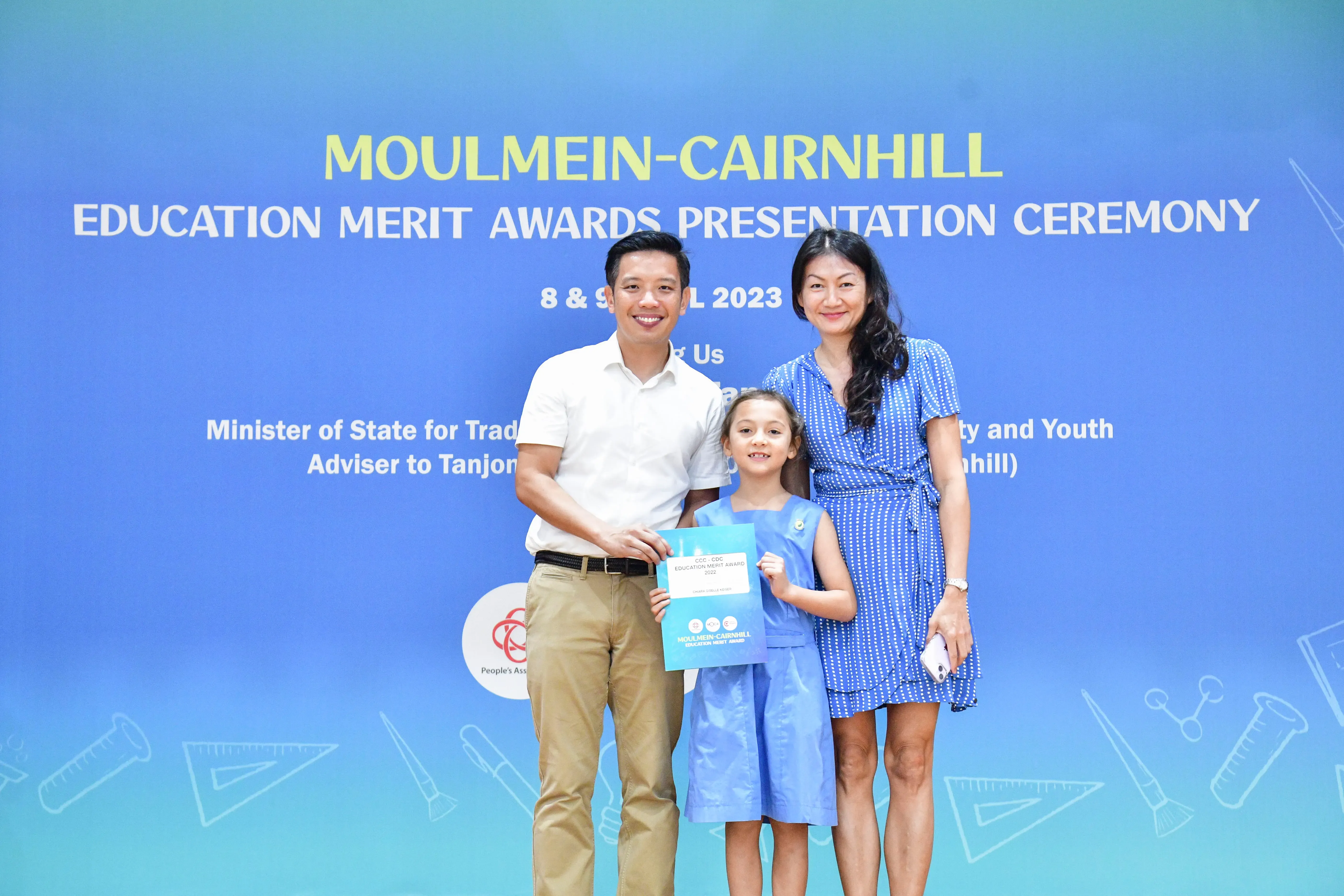 Two adults and a young girl pose with an award at the Moulmein-Cairnhill Education Merit Awards 2023.