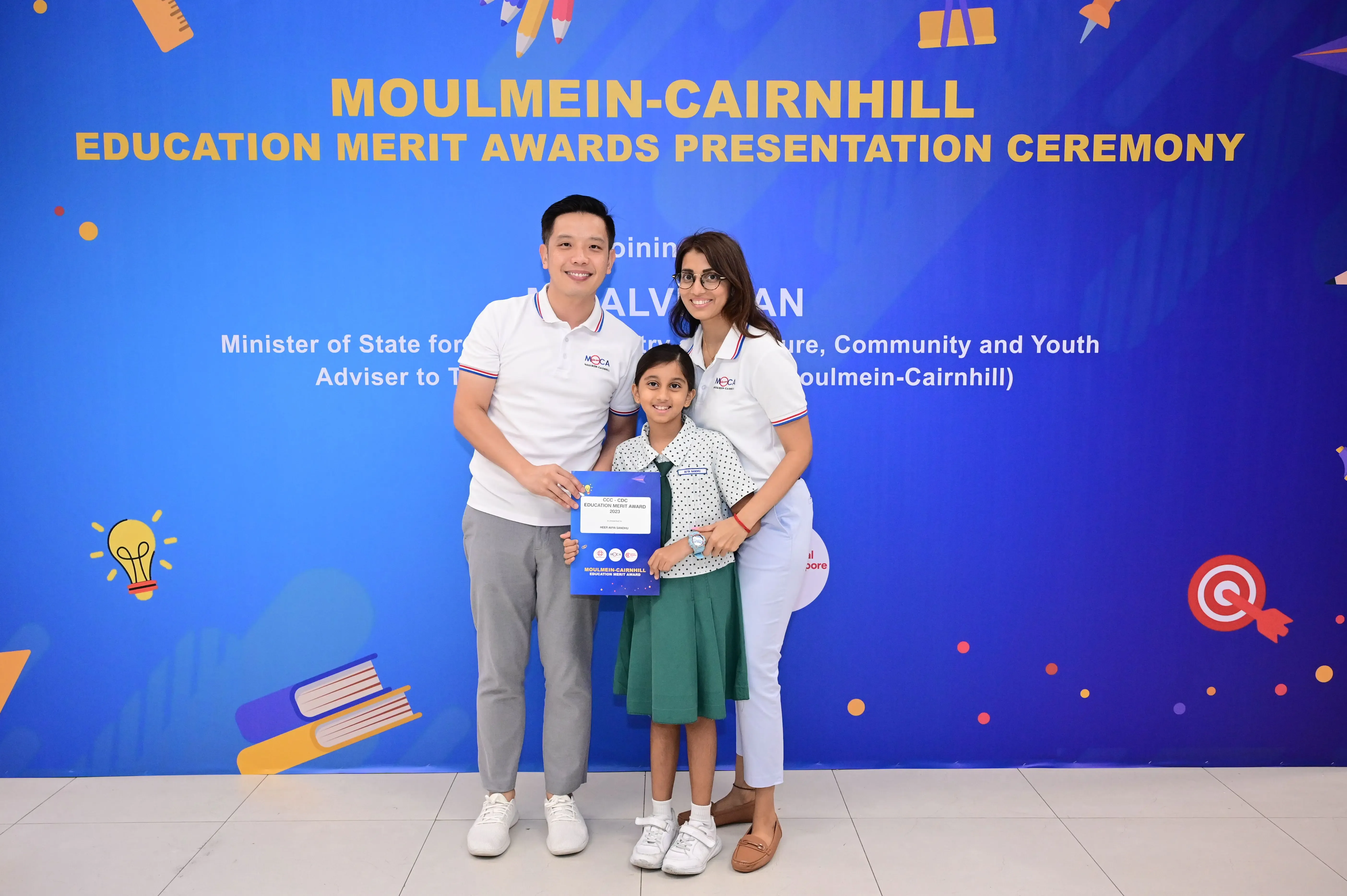 Two adults and a young girl hold an award certificate at the Moulmein-Cairnhill Education Merit Awards Ceremony.
