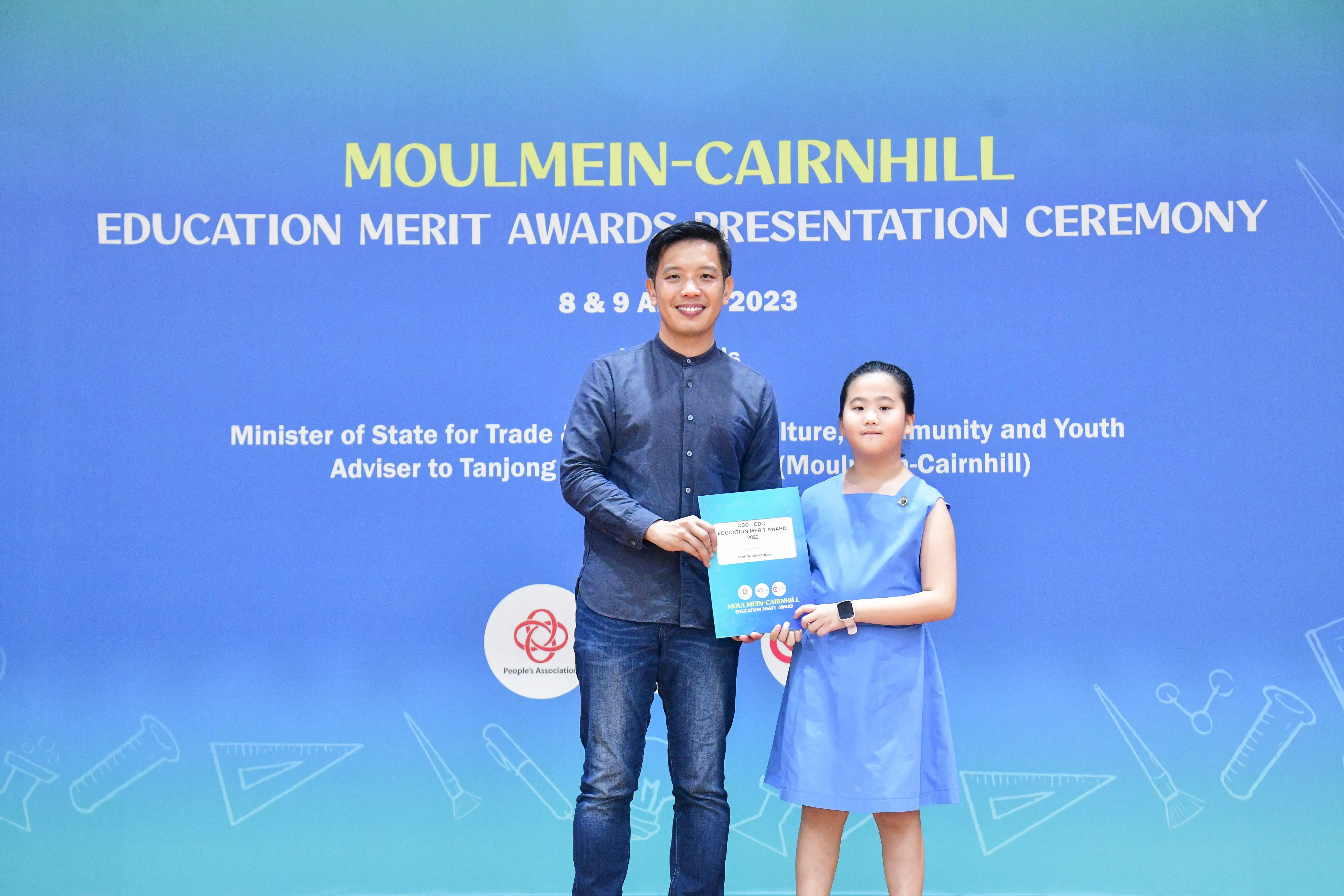 A man and a young girl hold a certificate together at the Moulmein-Cairnhill Education Merit Awards Ceremony 2023.