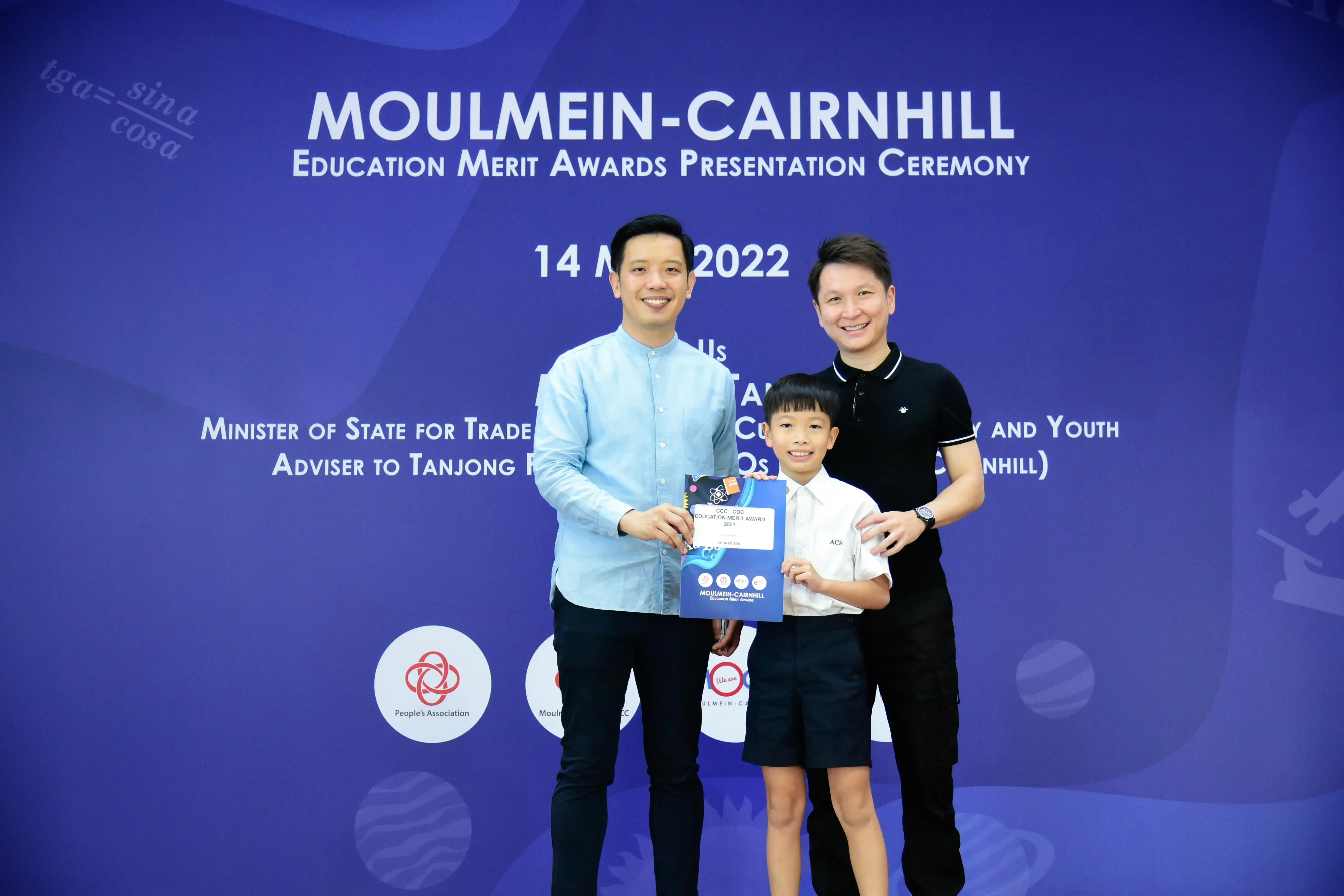Two adults and a young boy holding an award certificate at the Moulmein-Cairnhill Education Merit Awards 2022.