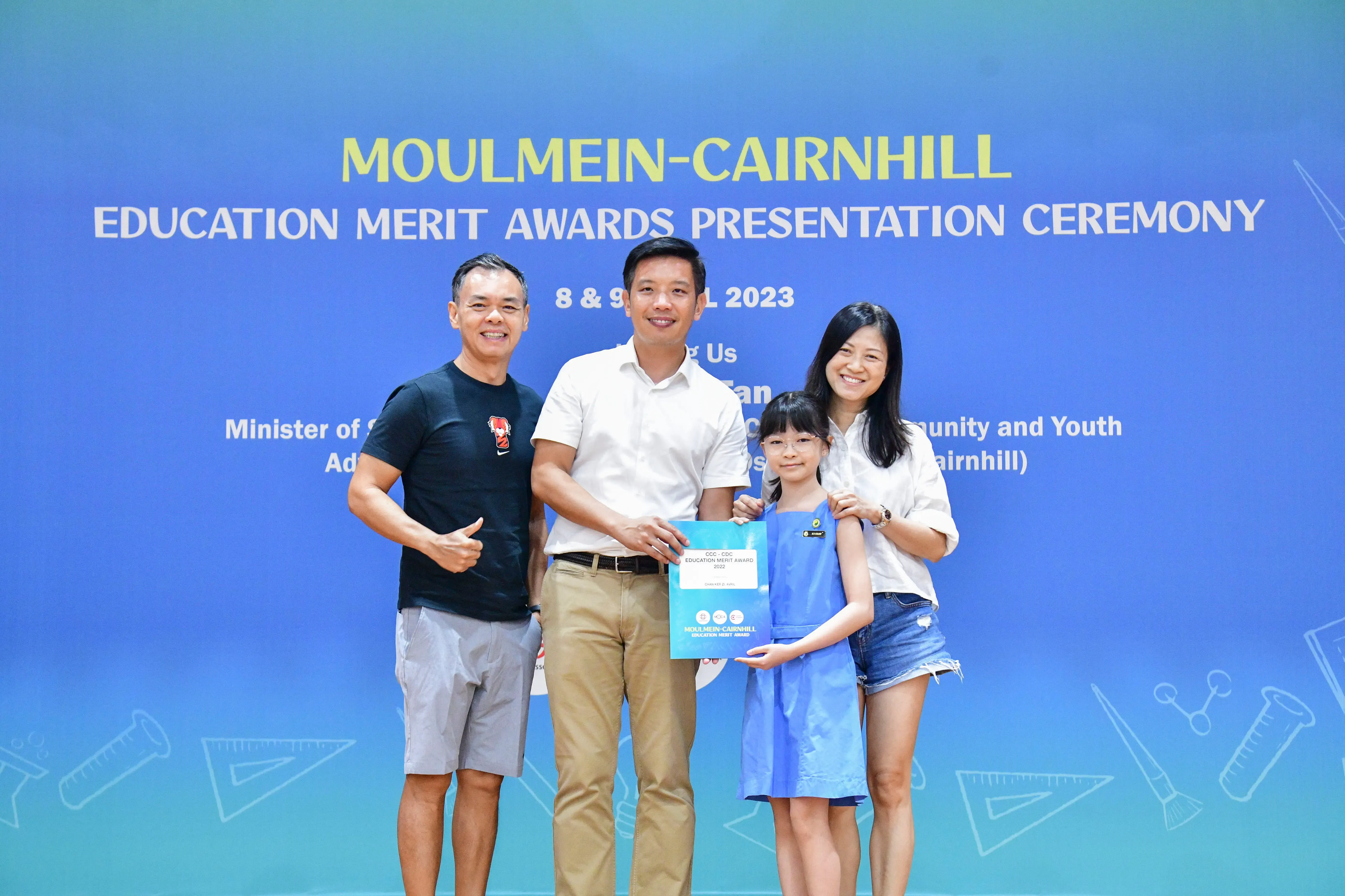 Three adults and a young girl pose with an award at the Moulmein-Cairnhill Education Merit Awards Ceremony 2023.