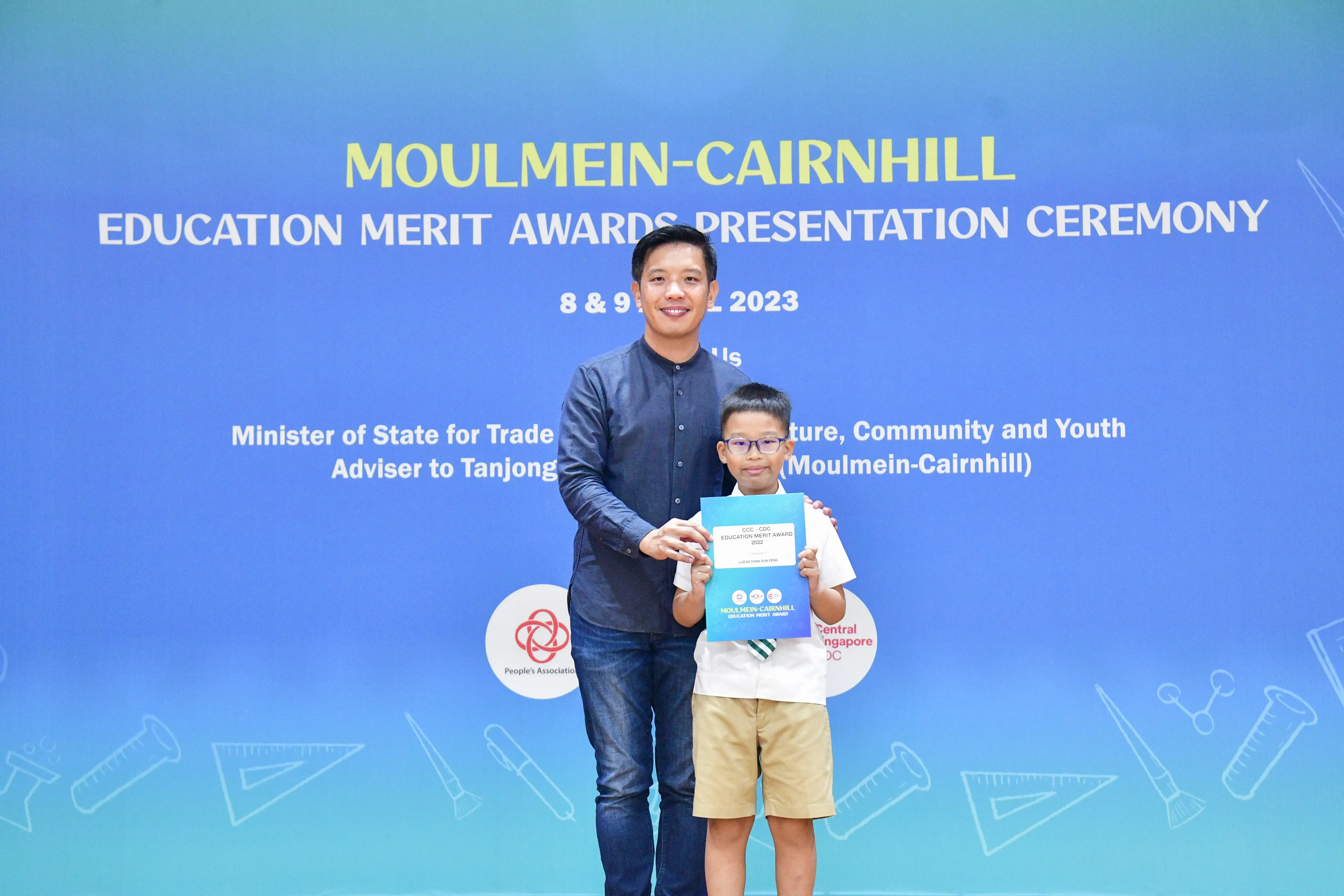 Man and young boy holding an award certificate at the Moulmein-Cairnhill Education Merit Awards Ceremony 2023.