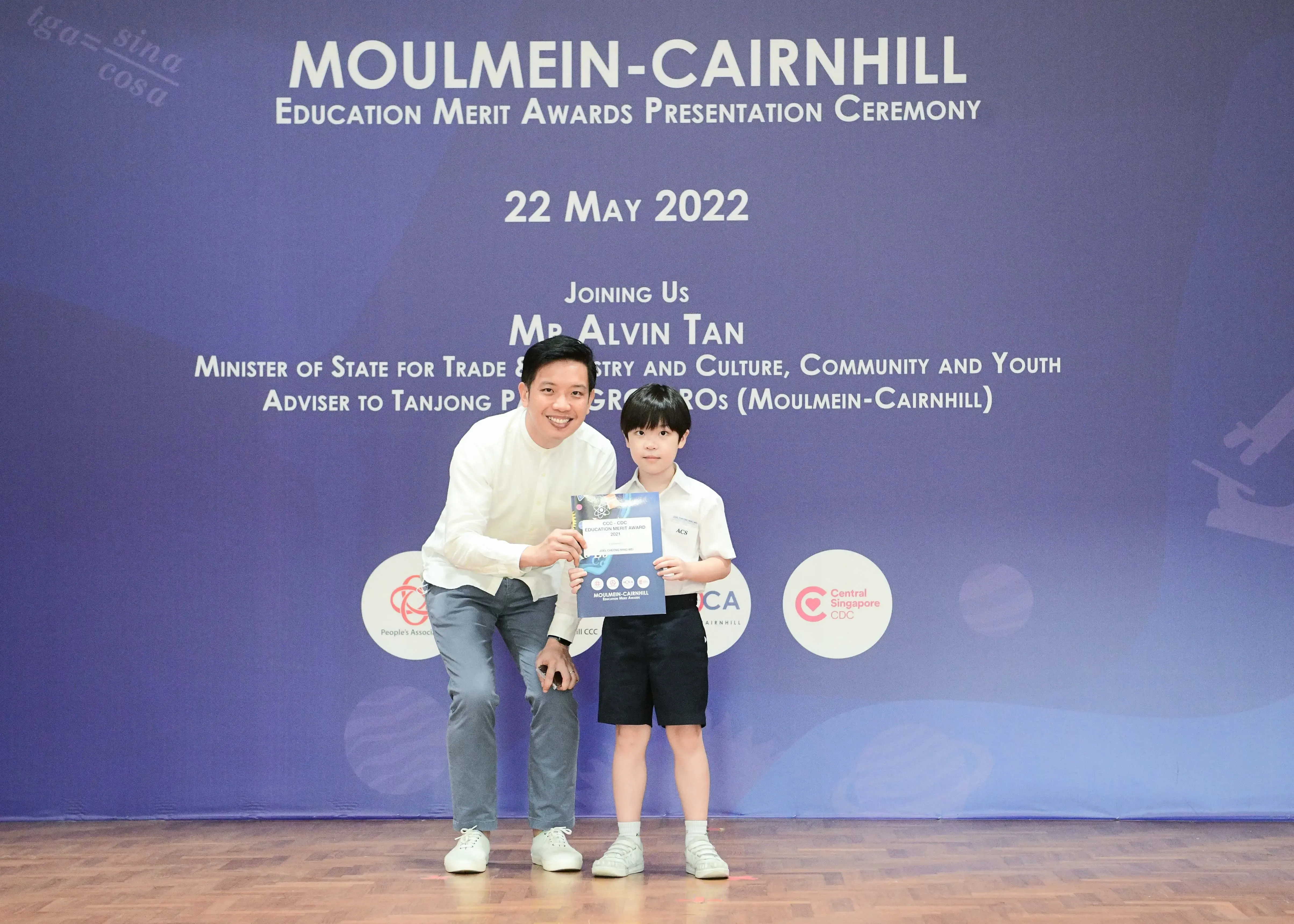 Adult man and young boy hold an award certificate at Moulmein-Cairnhill Education Merit Awards Ceremony, 22 May 2022.