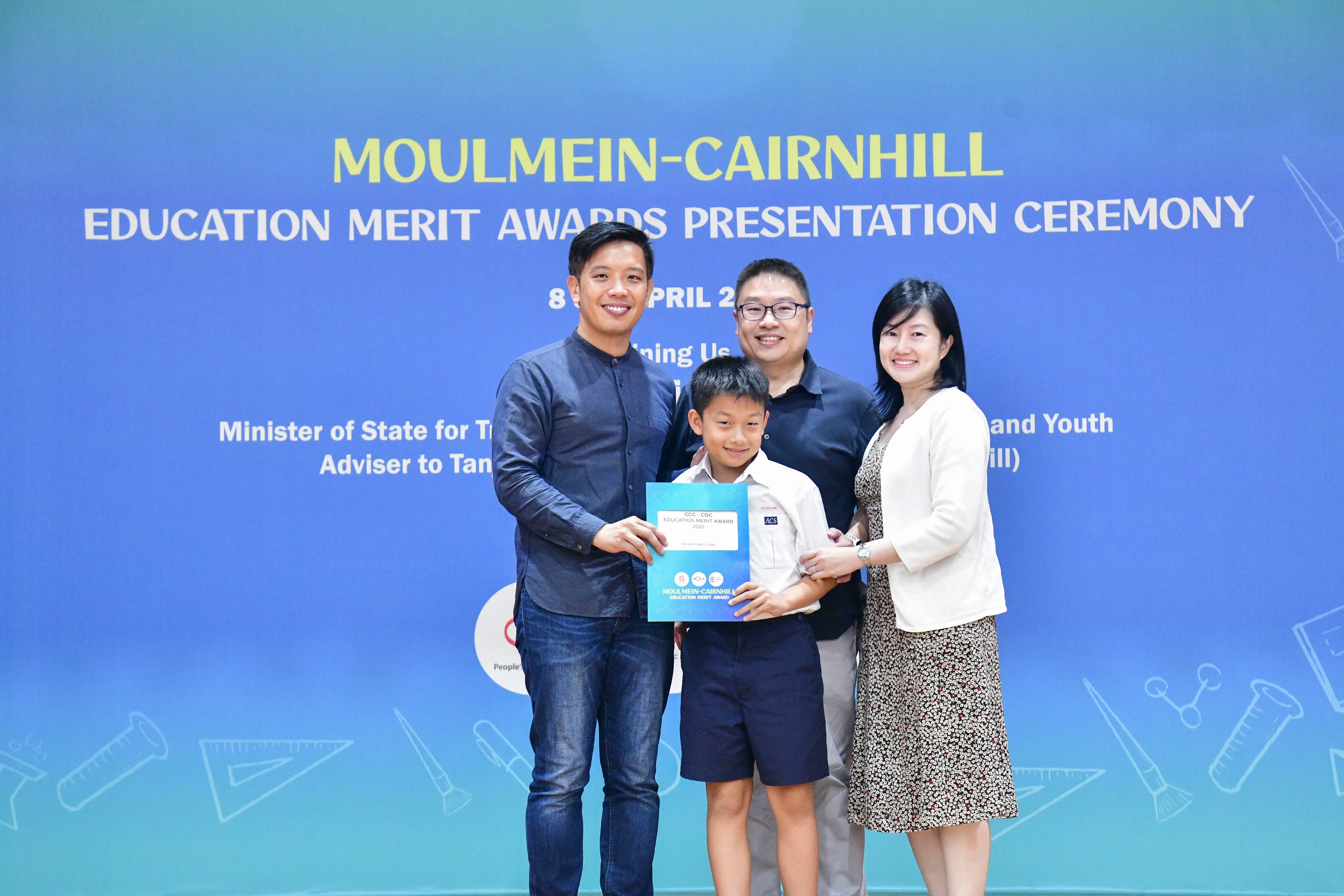 Three adults and a boy hold a certificate at the Moulmein-Cairnhill Education Merit Awards Presentation Ceremony.