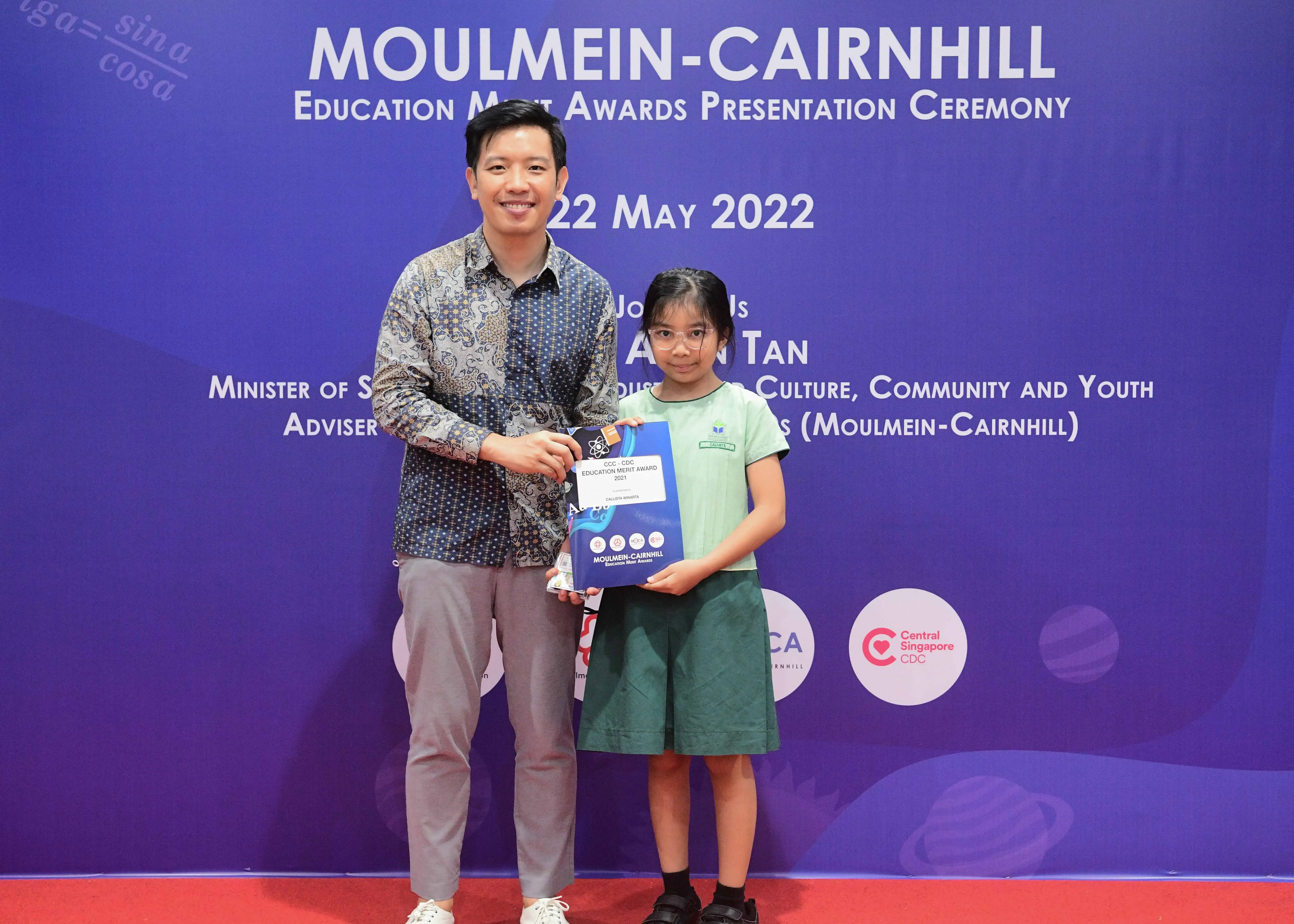 A man and a young girl hold an award certificate at the Moulmein-Cairnhill Education Merit Awards Ceremony, 22 May 2022.