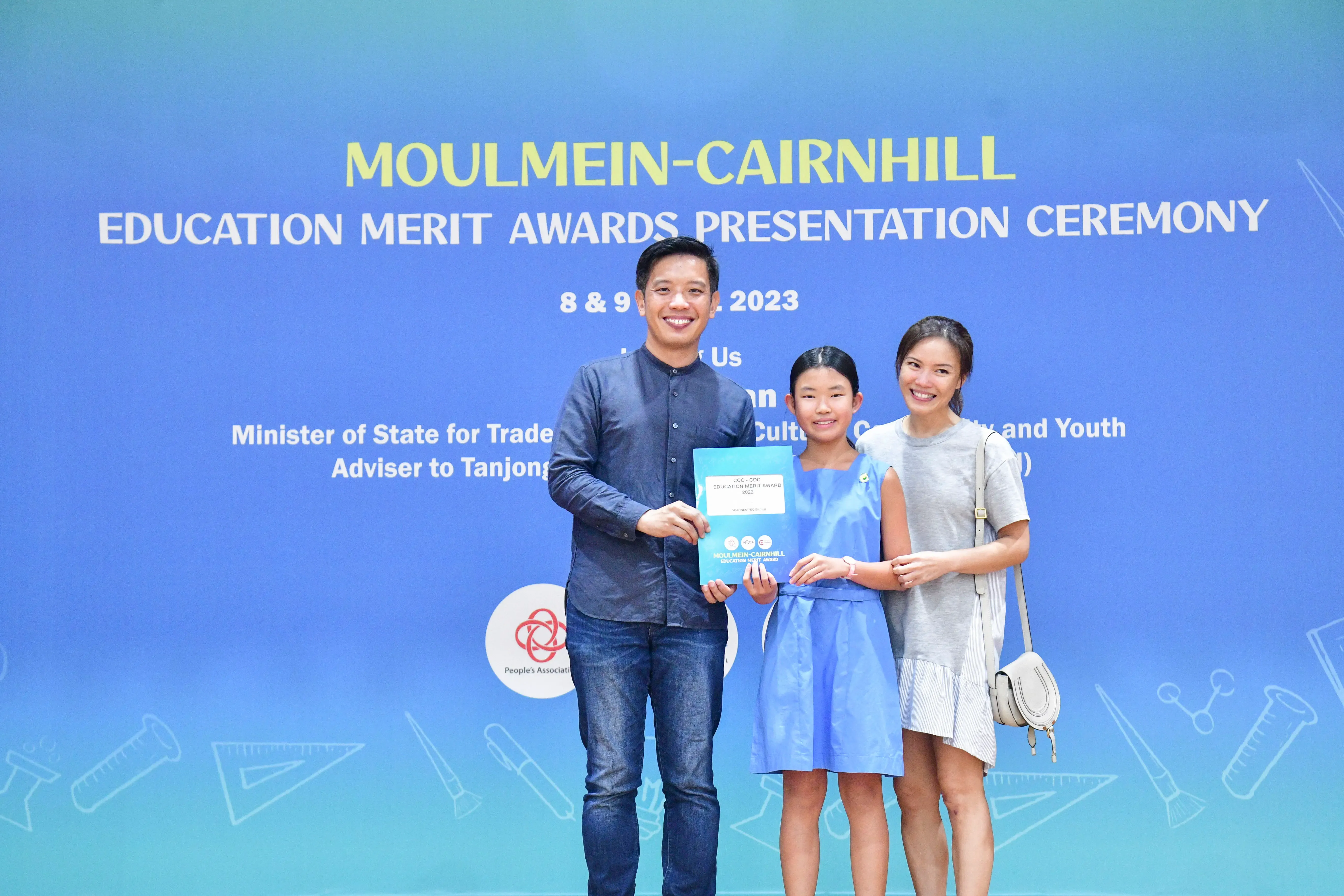 Three people smile while holding an award certificate at the Moulmein-Cairnhill Education Merit Awards Ceremony 2023.