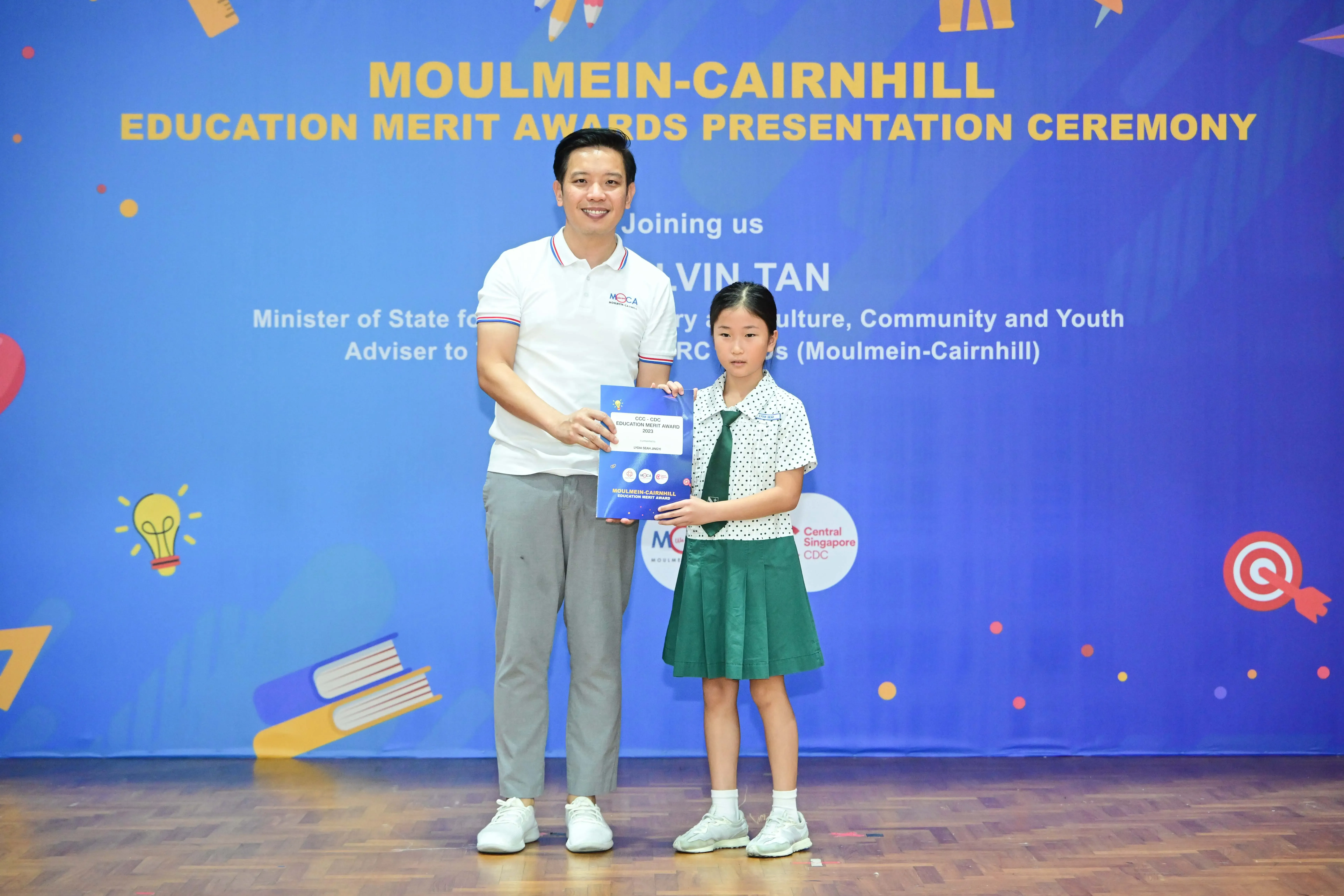 Man and young girl in school uniform hold a merit award certificate at Moulmein-Cairnhill Education Merit Awards ceremony.