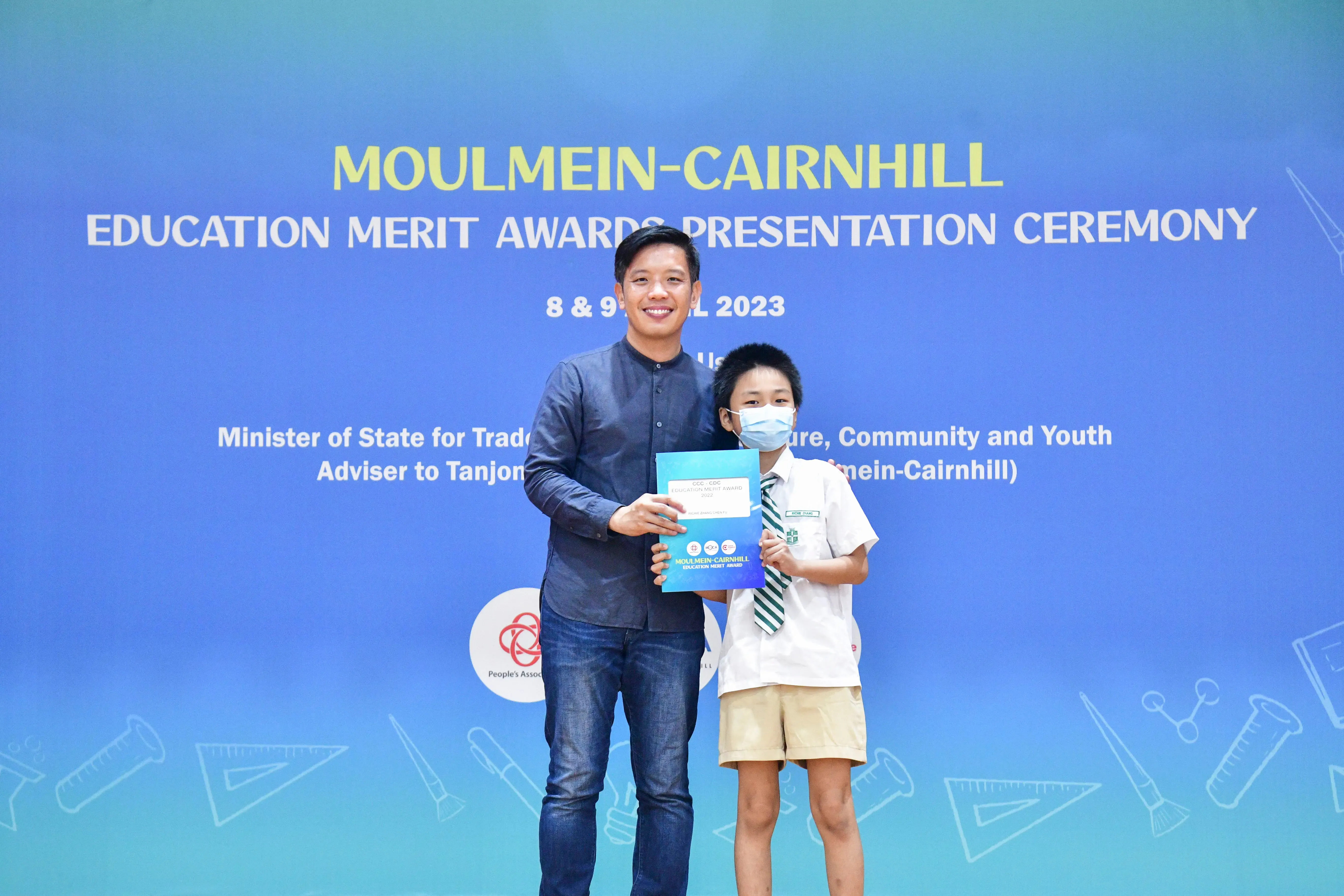 Adult and masked child hold an award certificate at the Moulmein-Cairnhill Education Merit Awards 2023.