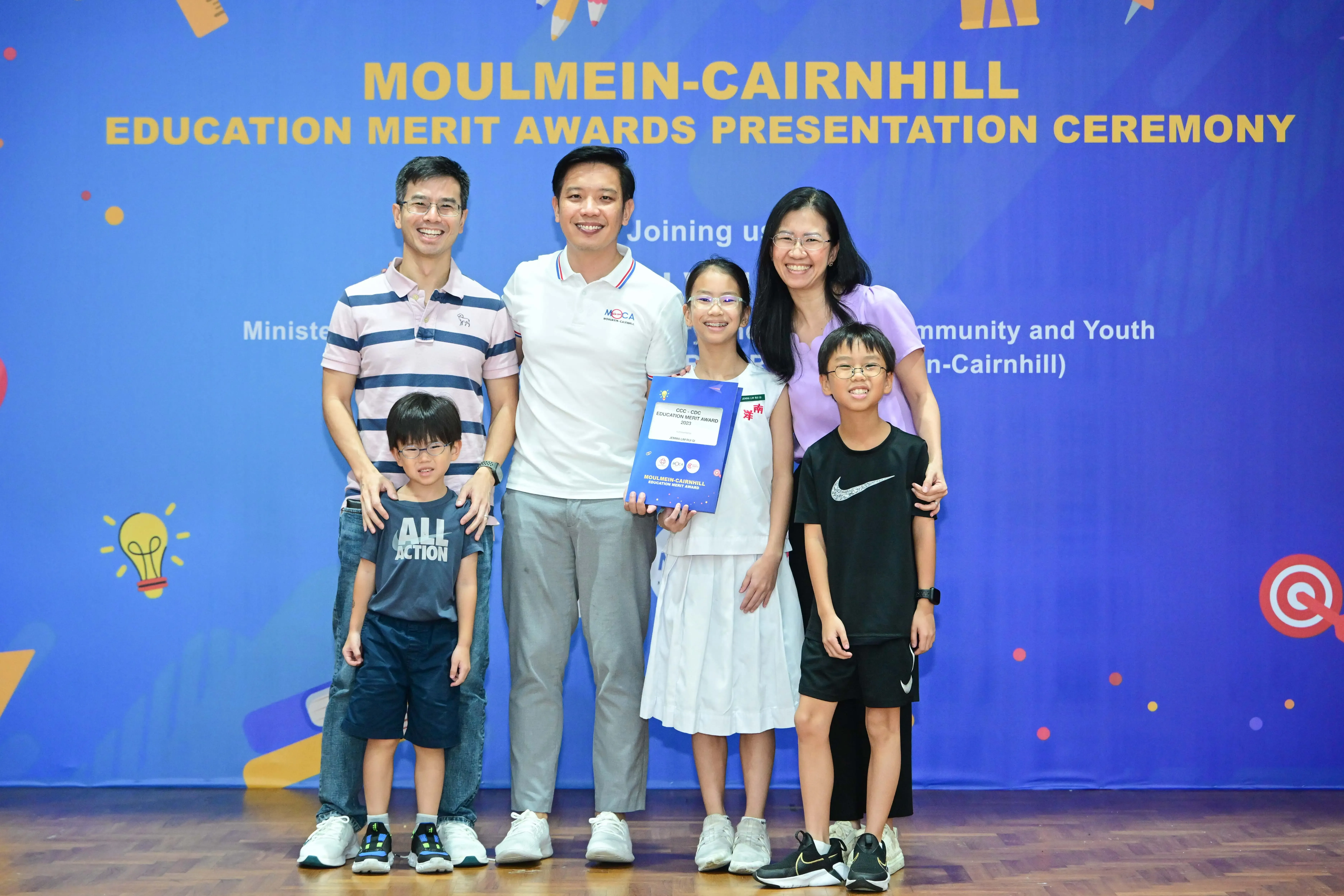 Group of adults and children smiling at the Moulmein-Cairnhill Education Merit Awards Presentation Ceremony.