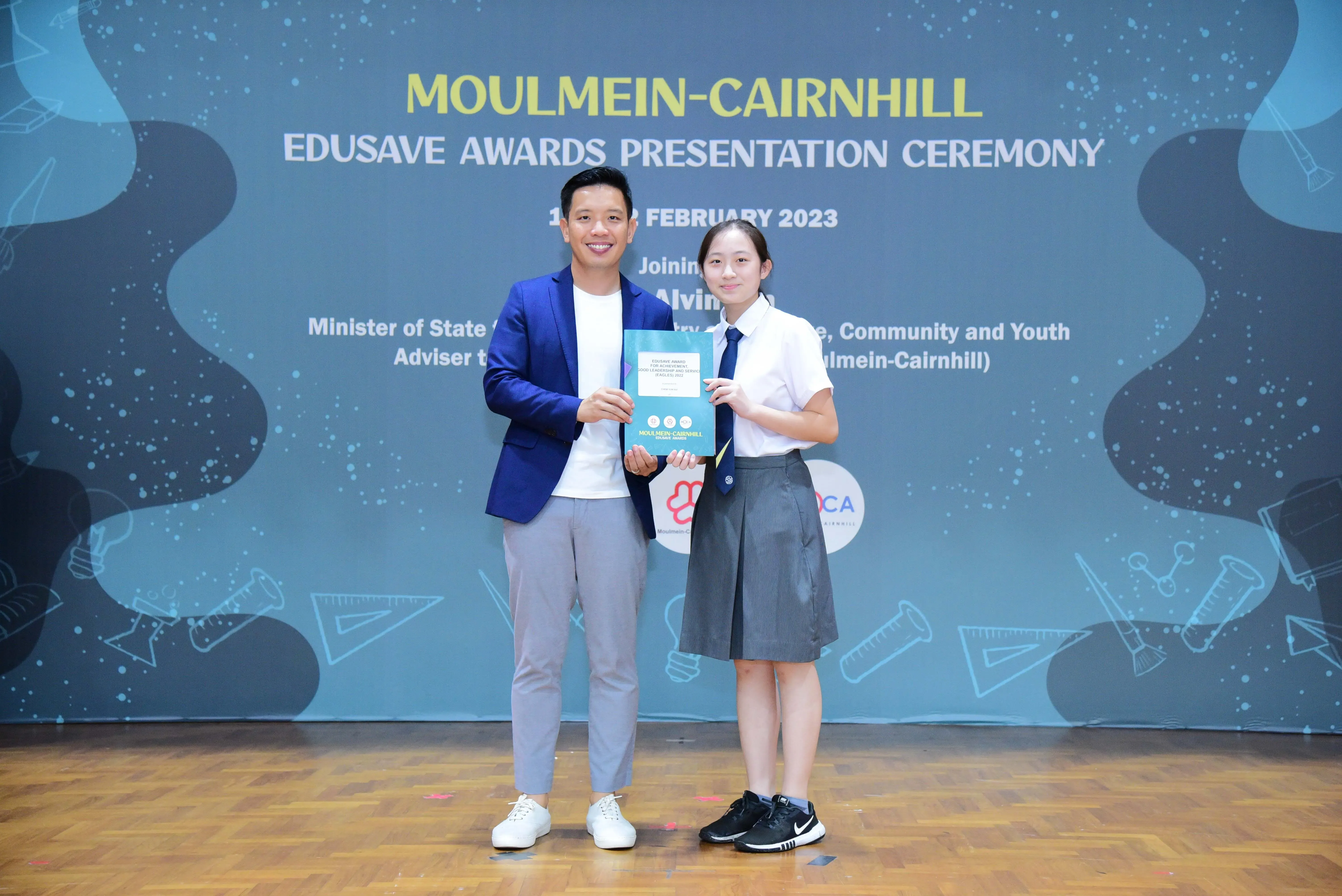 Two people hold a certificate at the Moulmein-Cairnhill Edusave Awards Presentation Ceremony, February 2023.