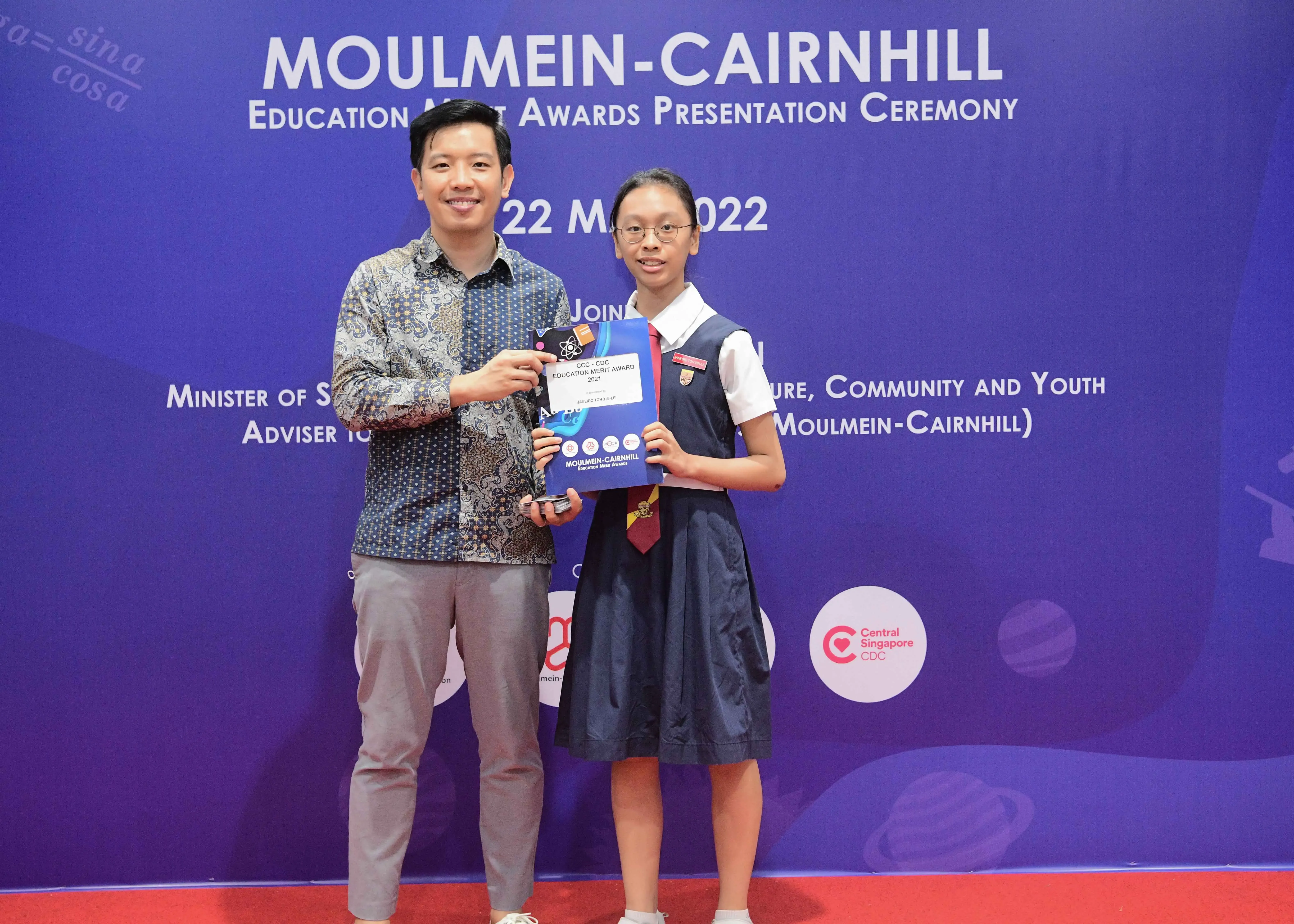 A man and a young student in school uniform pose holding an award at the Moulmein-Cairnhill Education Merit Awards 2022.