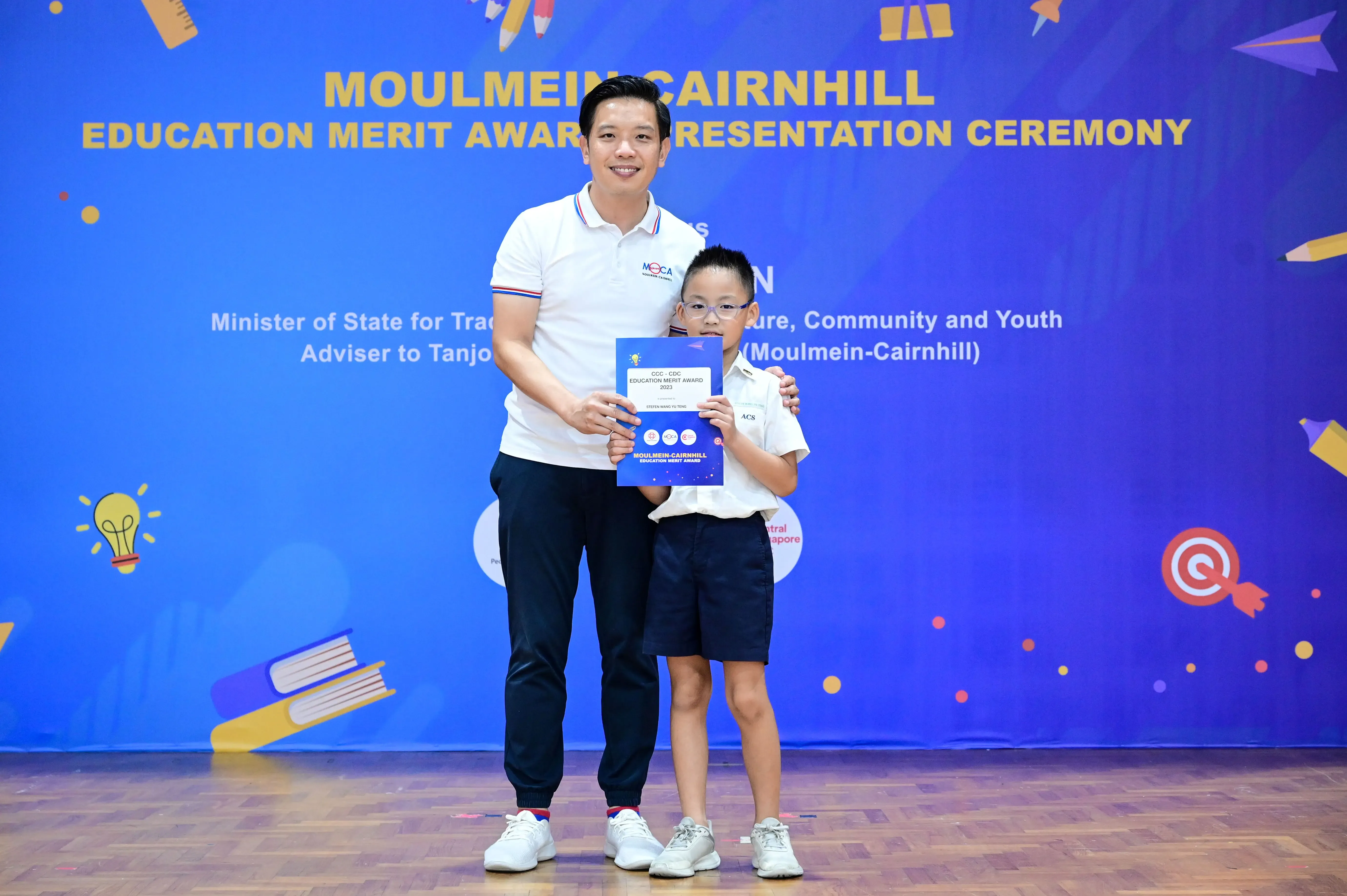 A man and a young boy holding an award certificate at the Moulmein-Cairnhill Education Merit Award Ceremony.