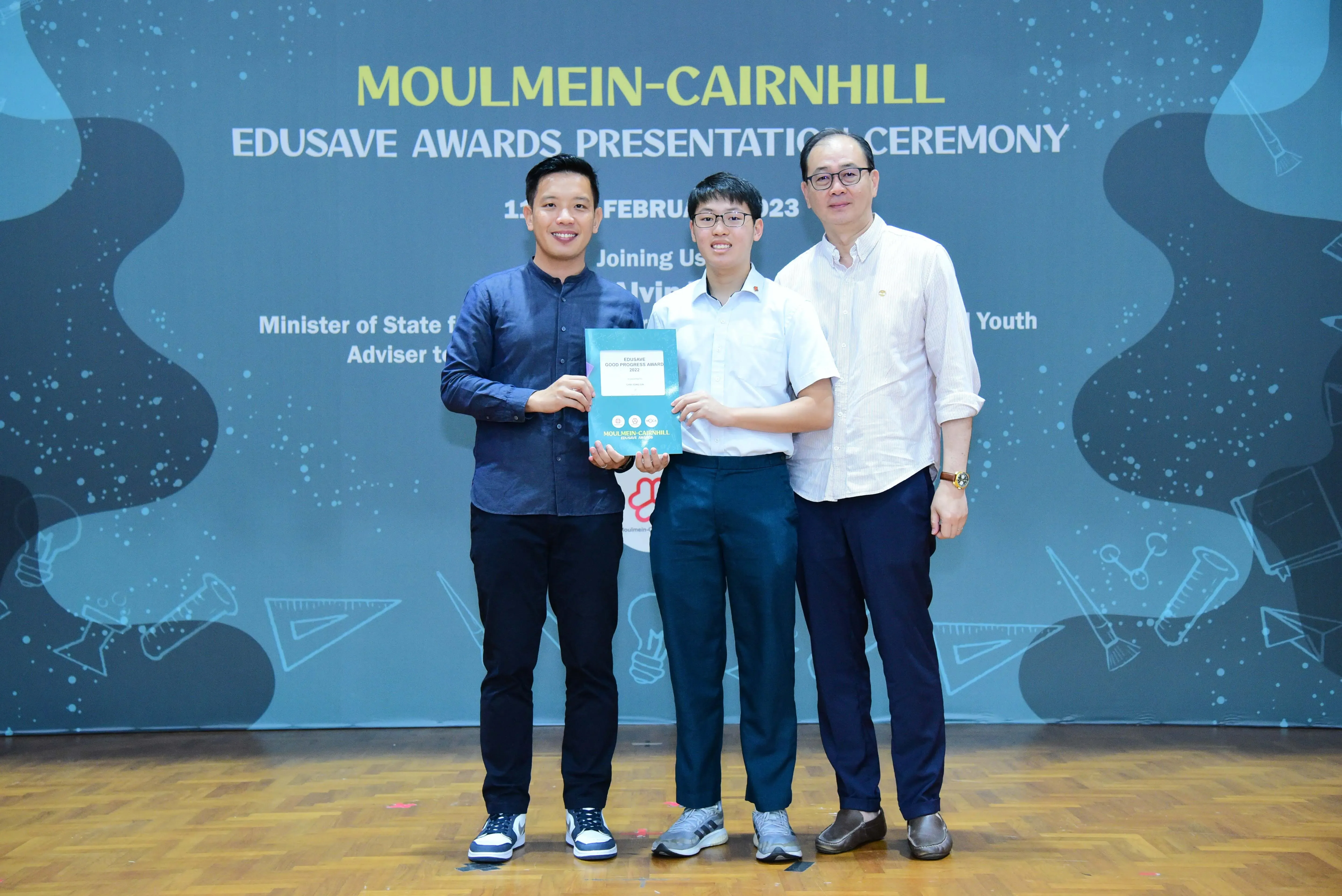Three men pose holding a certificate at the Moulmein-Cairnhill Edusave Awards Presentation Ceremony 2023.