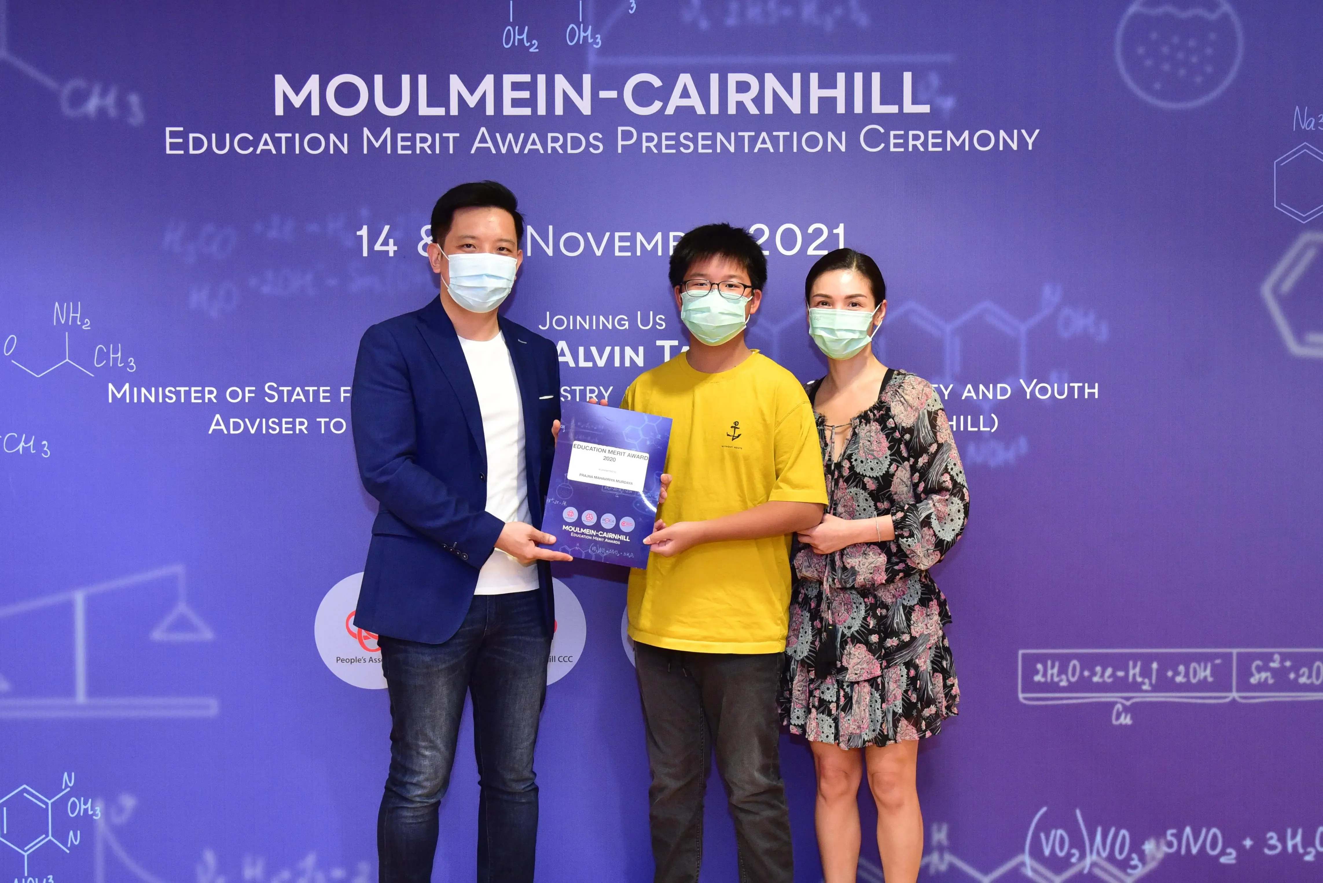 Three masked people hold an Education Merit Award at the Moulmein-Cairnhill ceremony, November 2021.