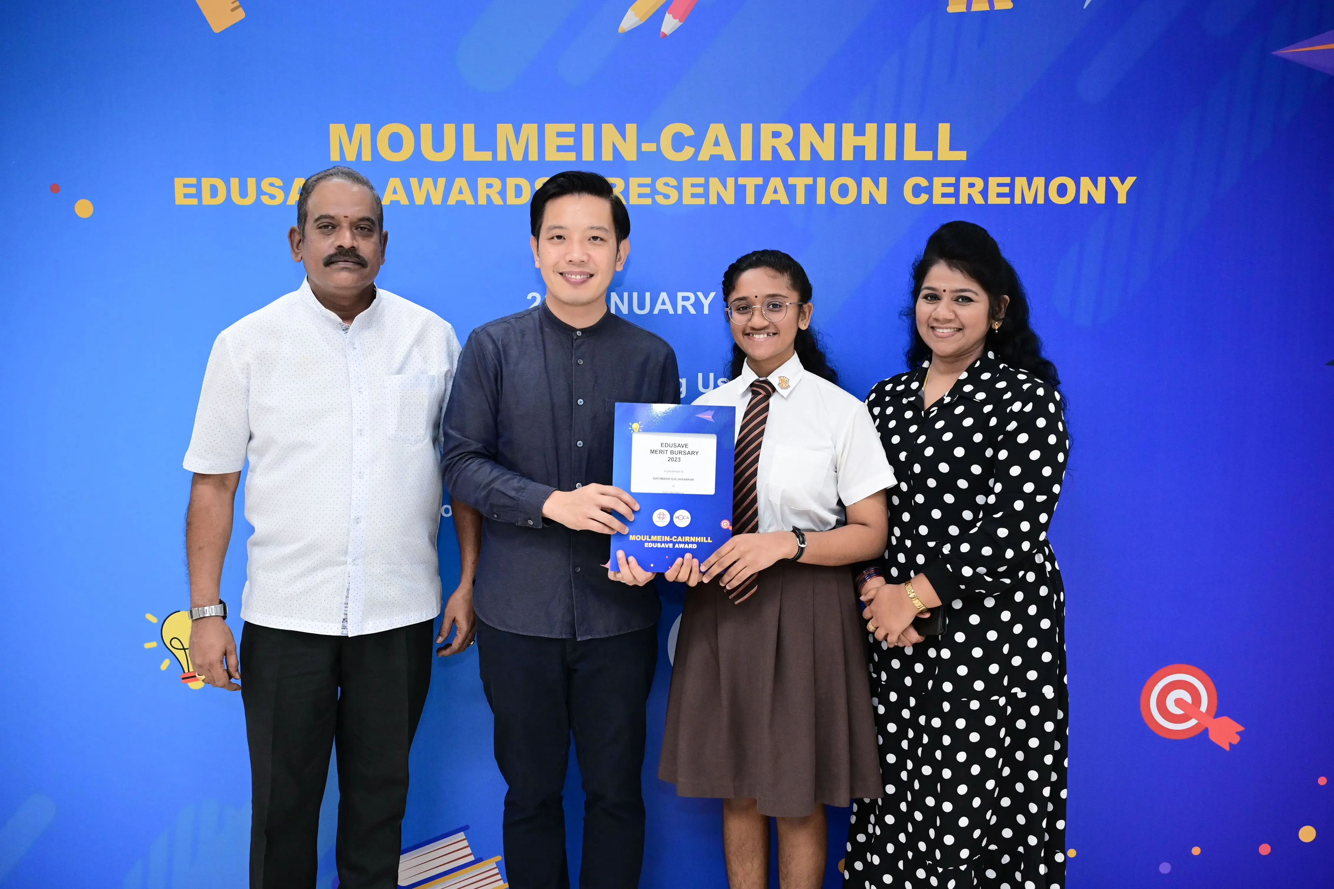 Four people posing at the Moulmein-Cairnhill Edusave Awards Presentation Ceremony, holding a blue award folder.