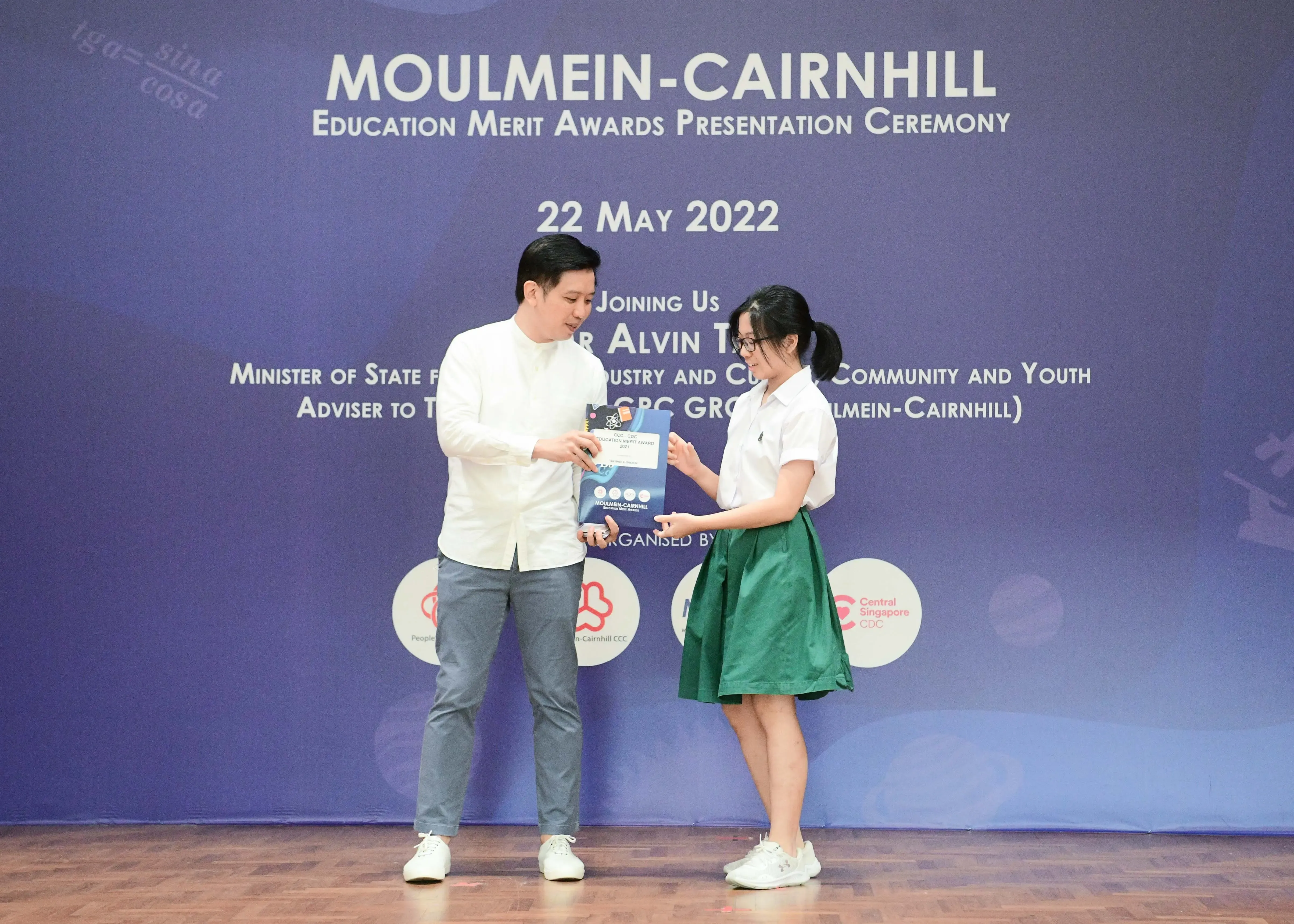A man in white shirt presents an award to a young girl in school uniform at the Moulmein-Cairnhill ceremony on 22 May 2022.