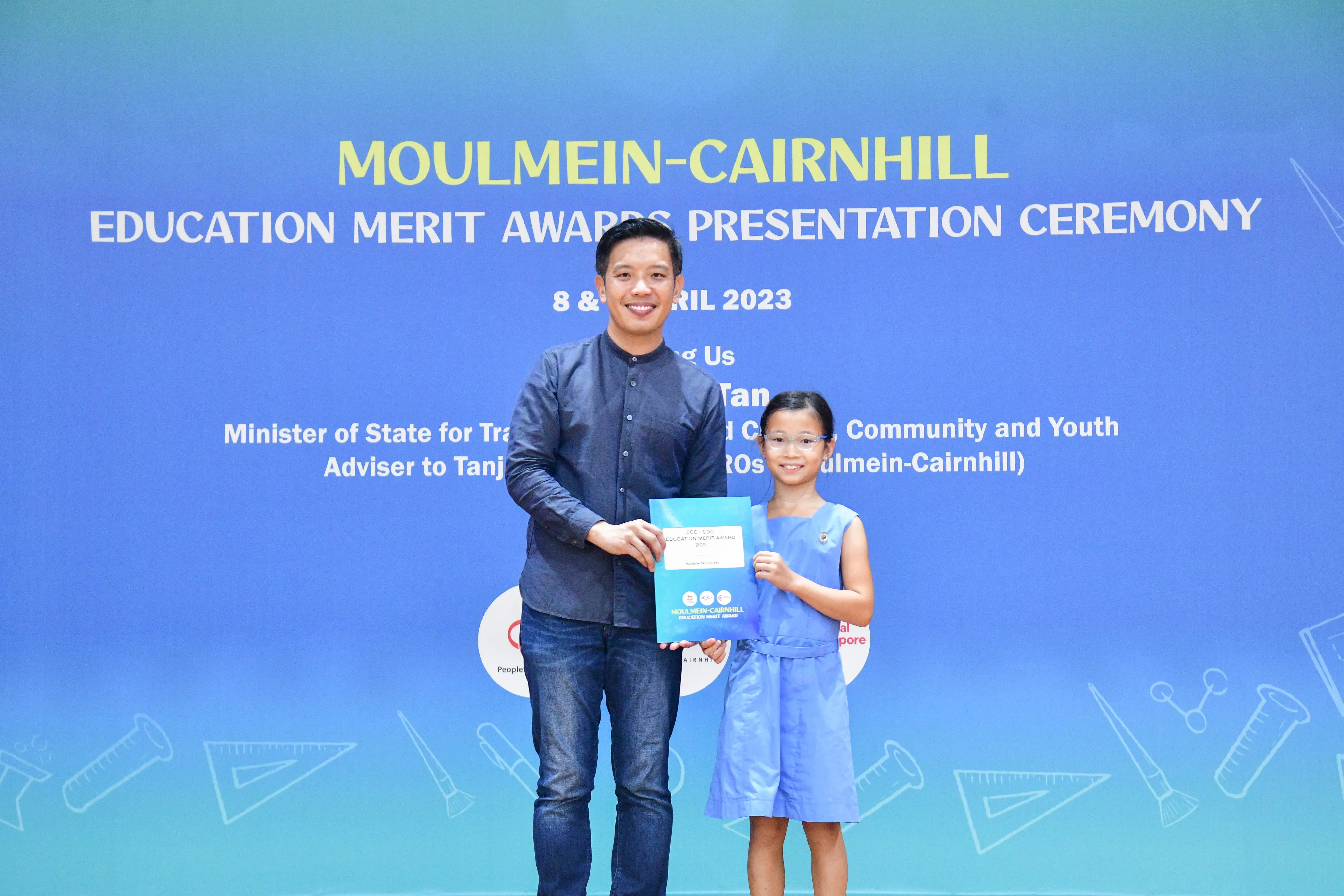 A man and a young girl hold an award certificate at the Moulmein-Cairnhill Education Merit Awards Ceremony, April 2023.