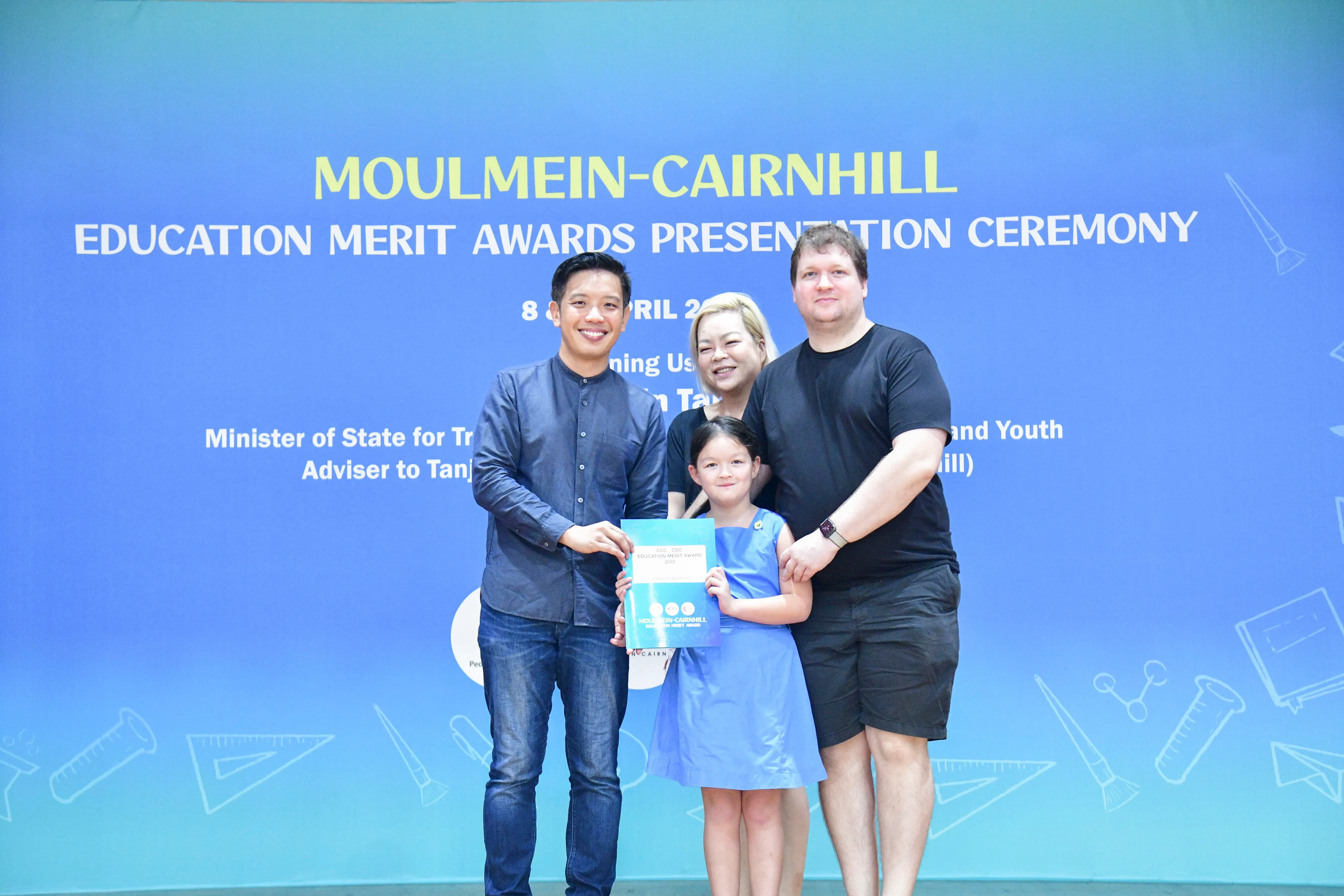 Three adults and a young girl hold an award certificate at the Moulmein-Cairnhill Education Merit Awards Presentation Ceremony.