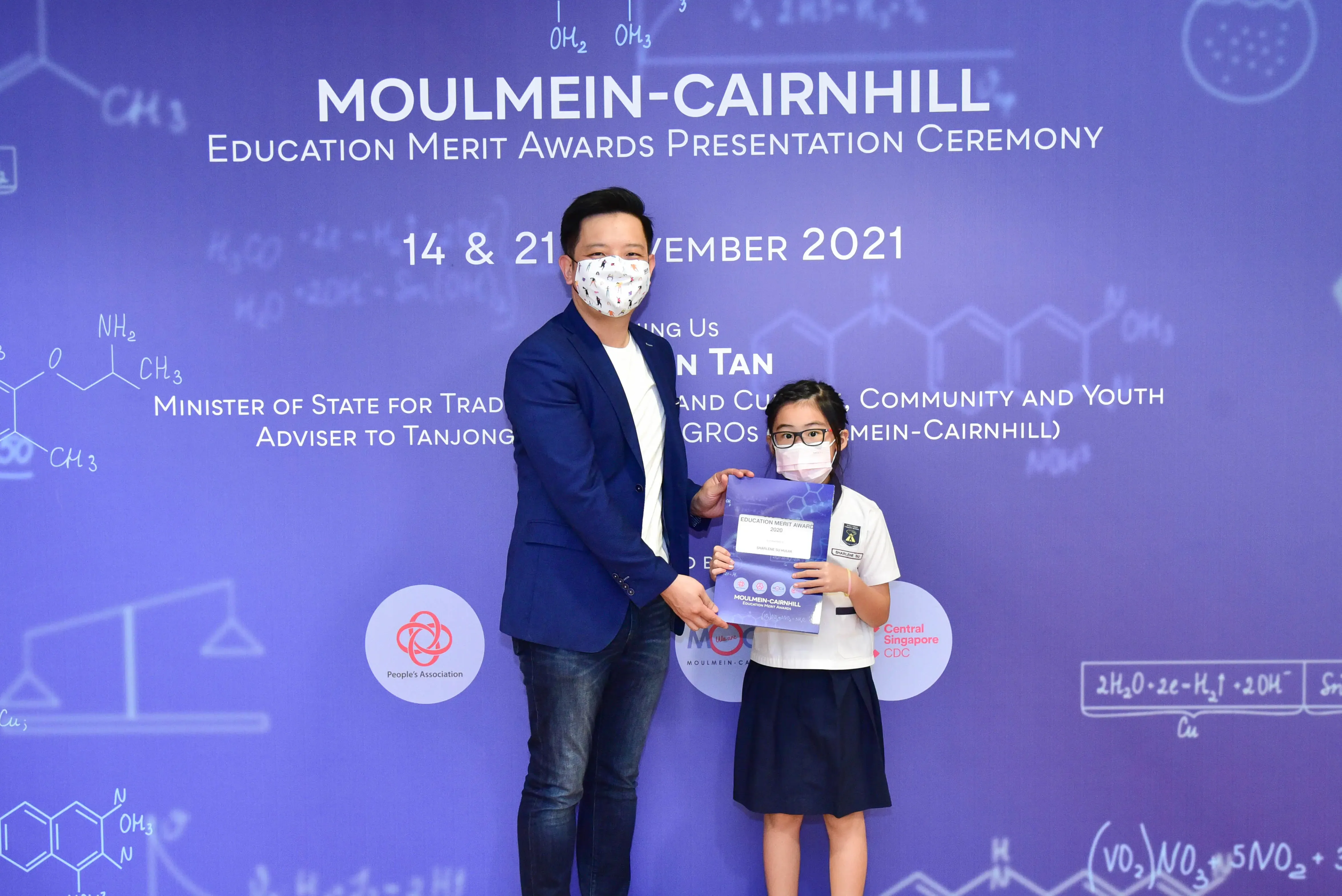 An adult and a young girl wearing masks hold an award folder at the Moulmein-Cairnhill Education Merit Awards 2021.