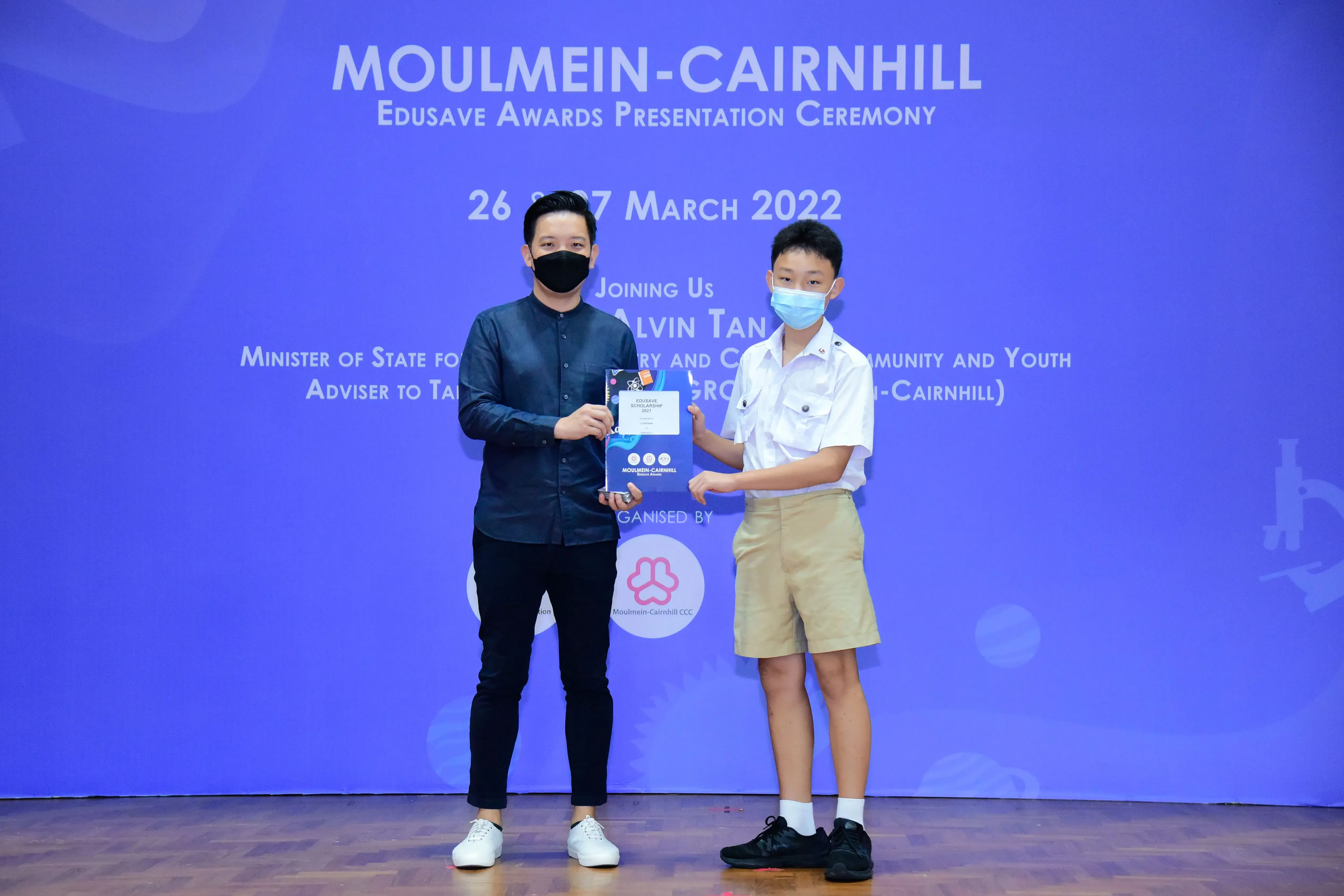 Two masked individuals hold a certificate at the Moulmein-Cairnhill Edusave Awards Ceremony, March 2022.