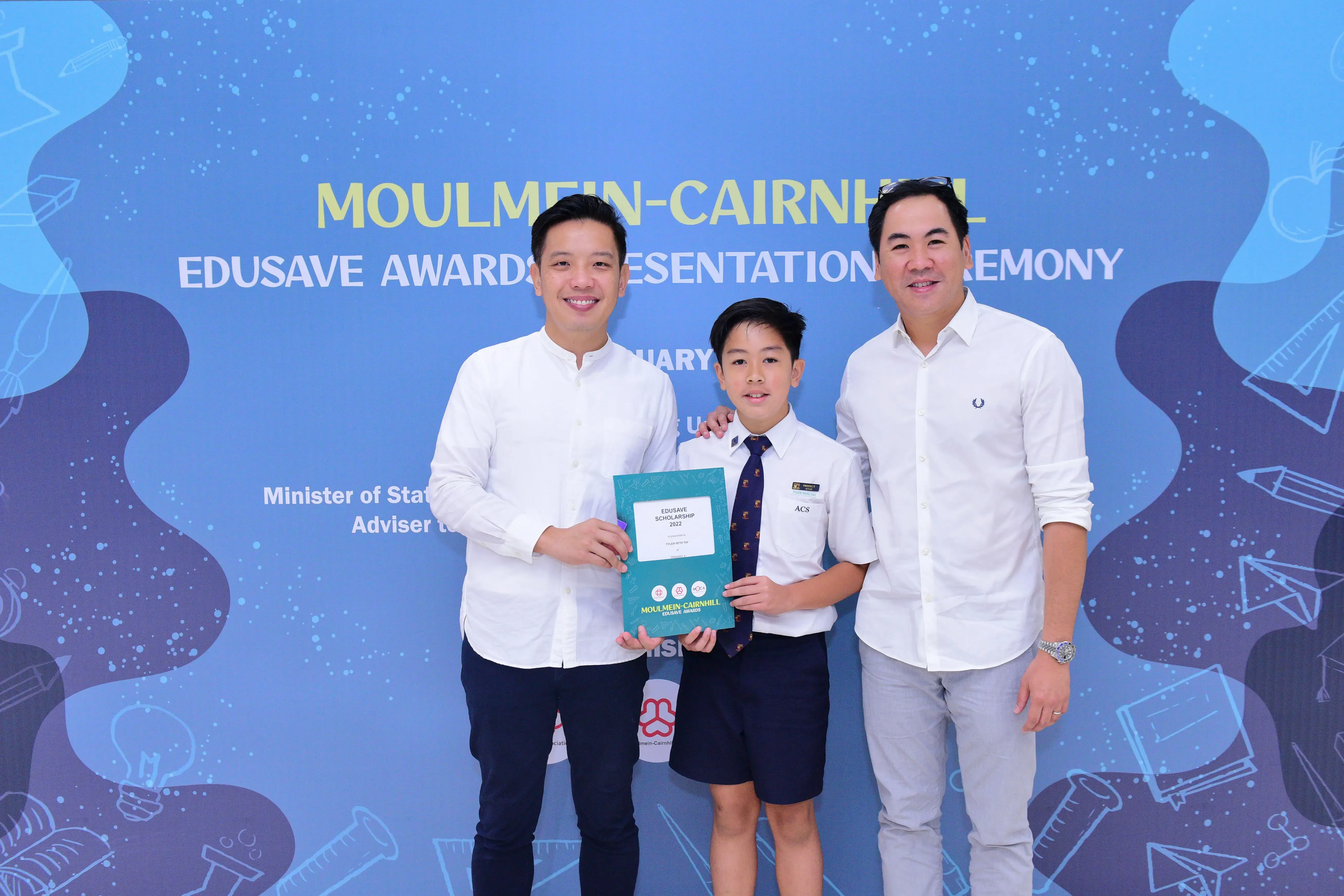 Two men and a boy in school uniform hold a certificate at the Moulmein-Cairnhill Edusave Awards Ceremony.