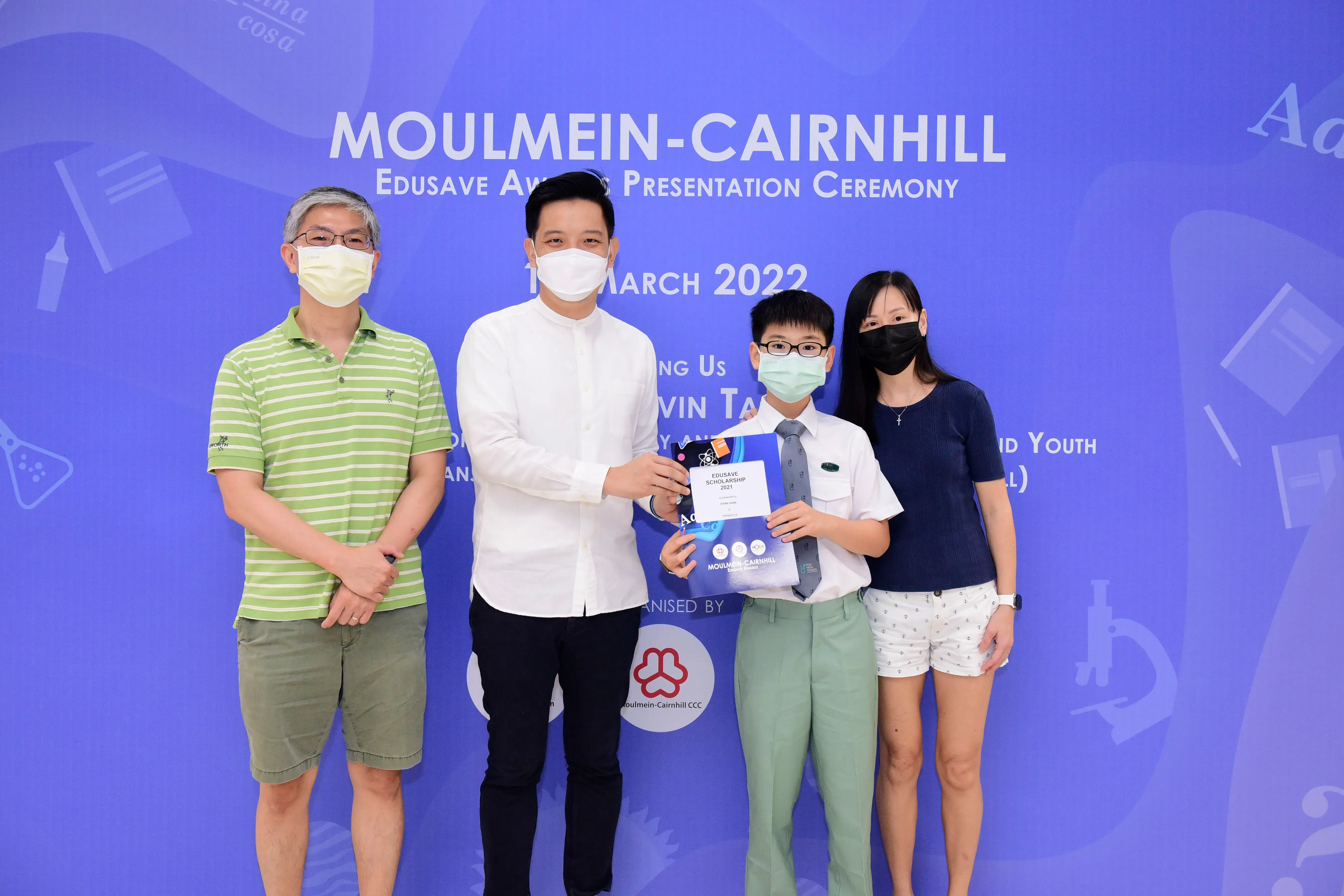 Four masked people pose at the Moulmein-Cairnhill Edusave Award Presentation Ceremony, March 2022, holding a certificate.