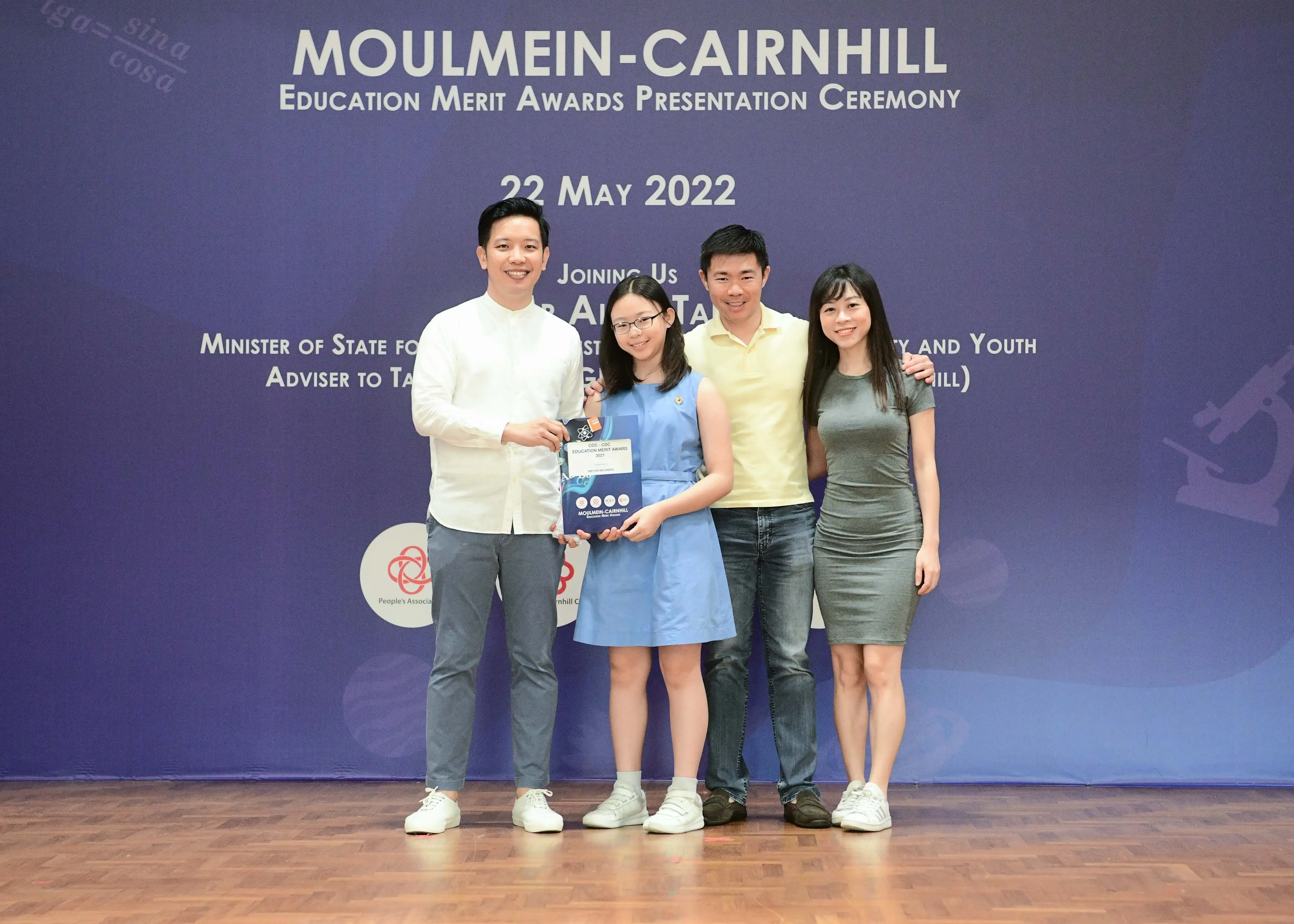 Four people pose at the Moulmein-Cairnhill Education Merit Awards Ceremony on 22 May 2022, with a girl holding an award.