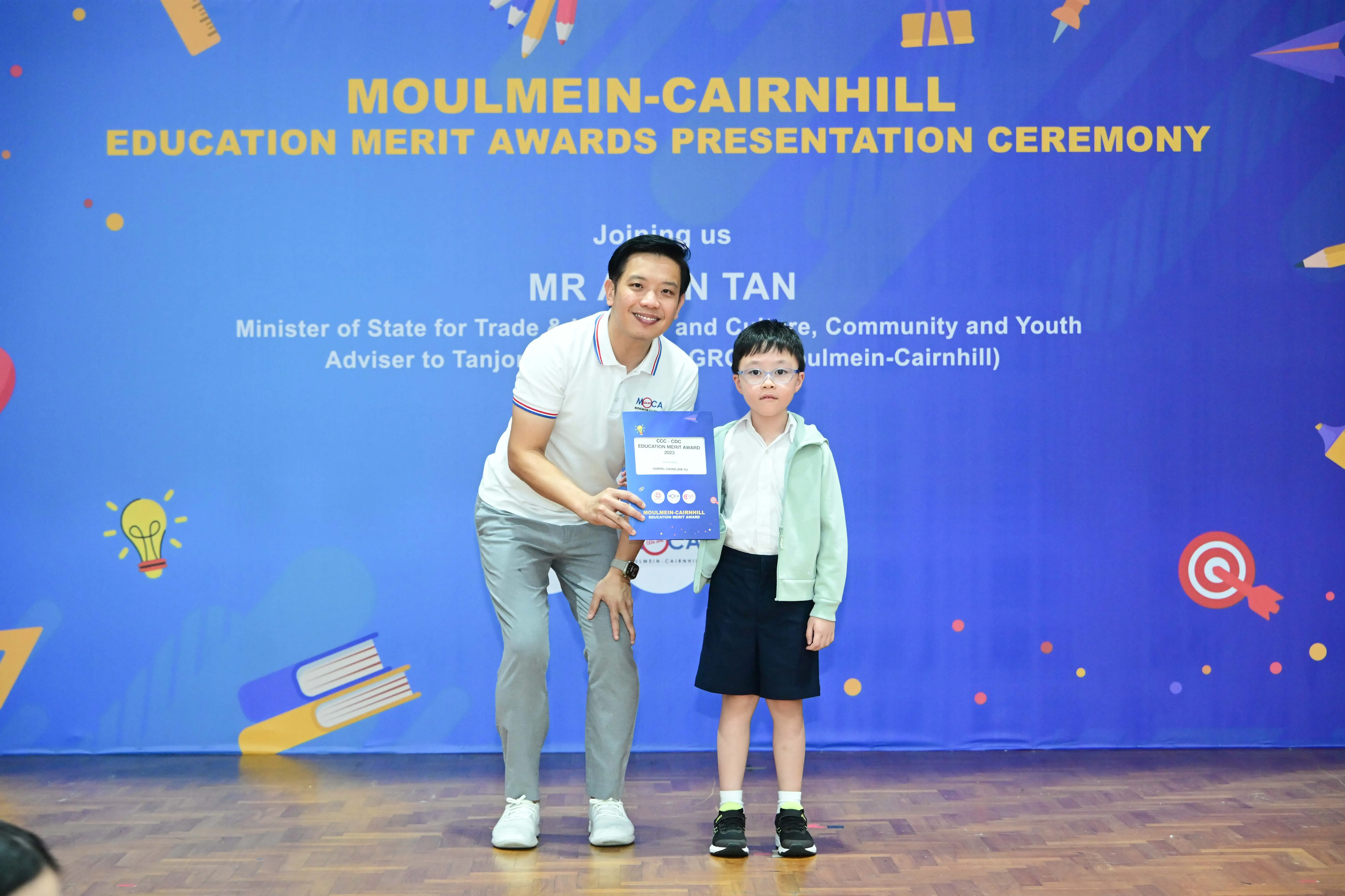 A man and a young boy hold an award certificate at the Moulmein-Cairnhill Education Merit Awards Presentation Ceremony.