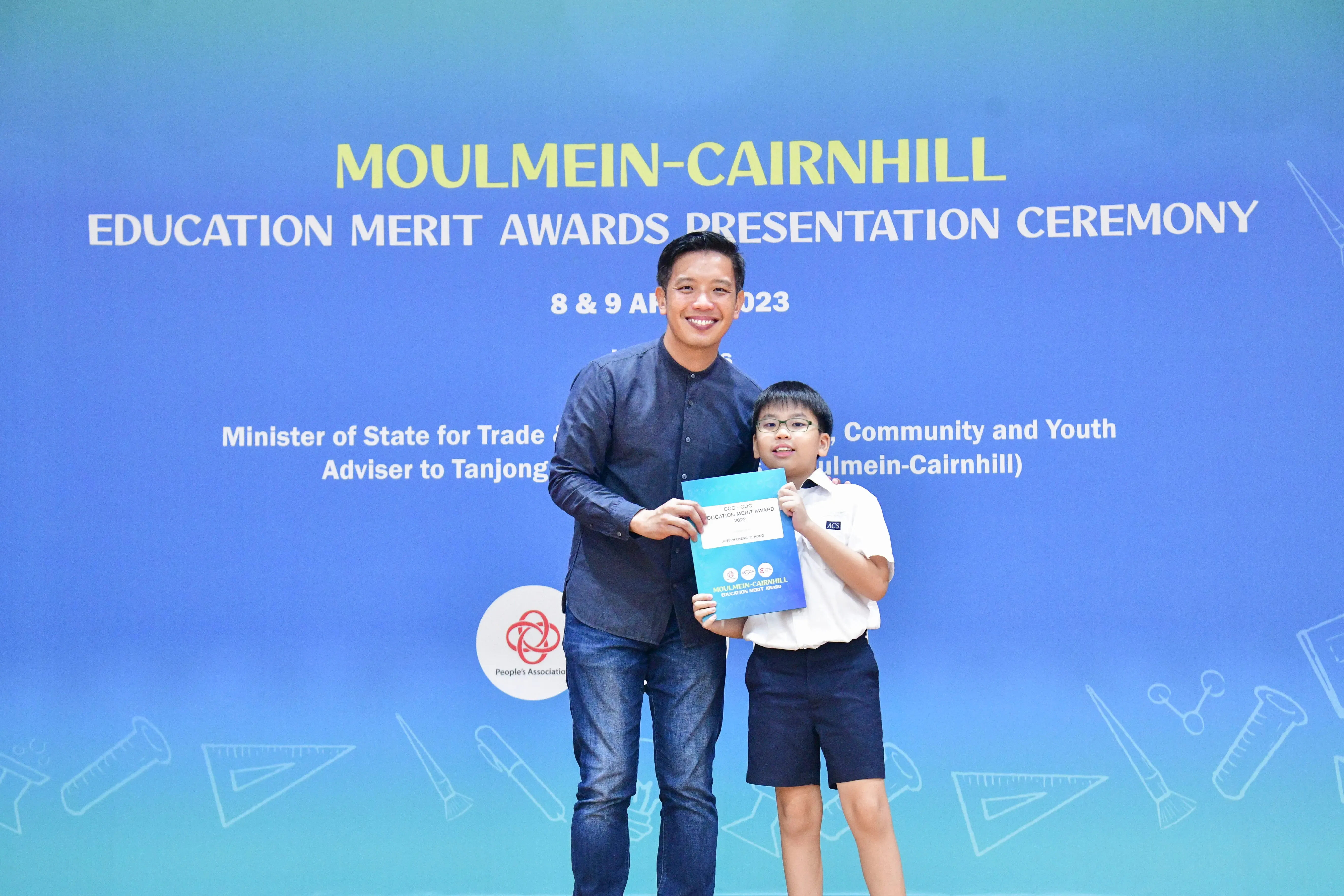 An adult and a young student hold an award certificate at the Moulmein-Cairnhill Education Merit Awards Ceremony 2023.