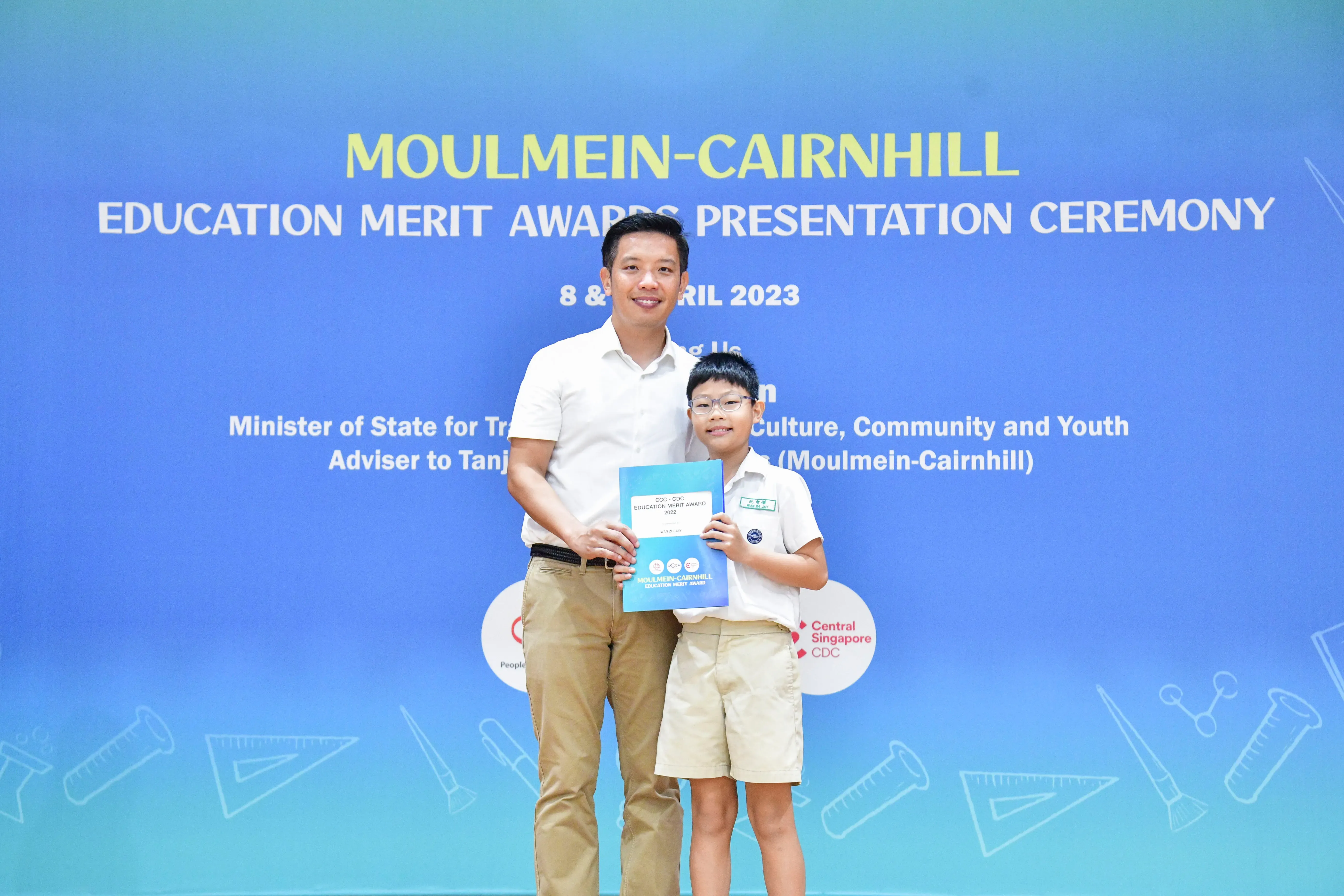 A man and a young boy in school uniform hold an award certificate at the Moulmein-Cairnhill Education Merit Awards 2023.