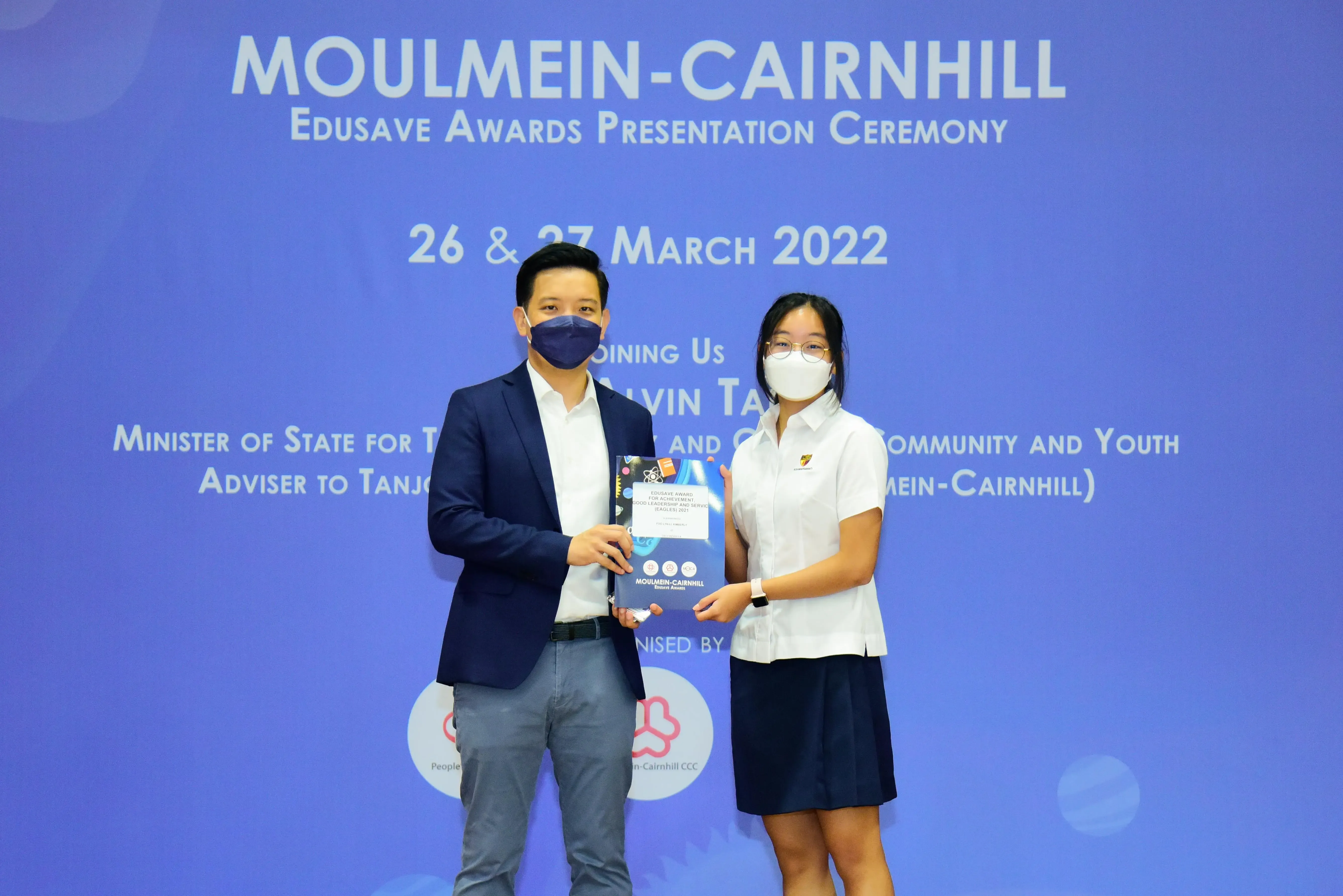 Two masked people hold a certificate at the Moulmein-Cairnhill Edusave Awards Presentation Ceremony, March 2022.