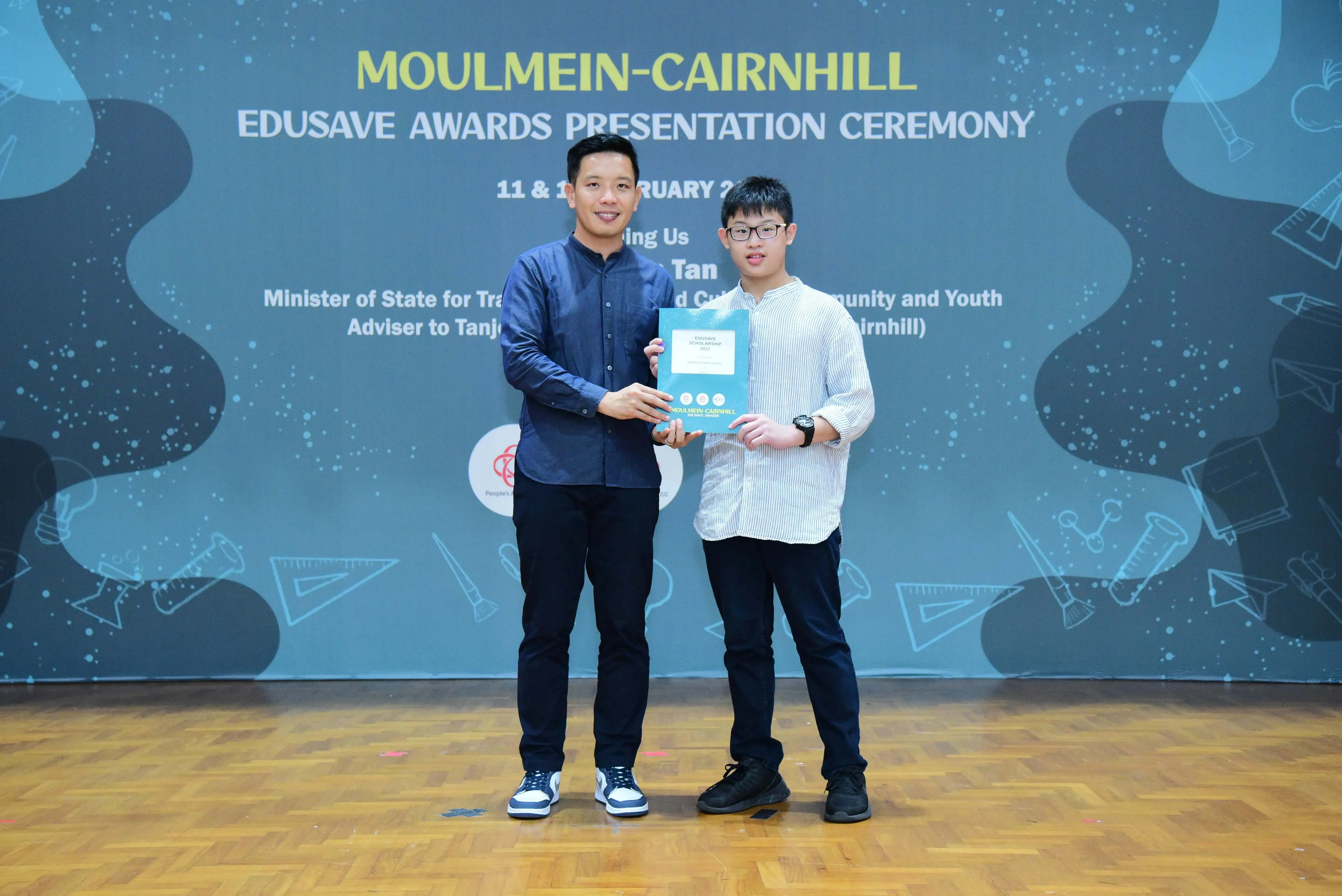 Two men hold a certificate together at the Moulmein-Cairnhill Edusave Awards Presentation Ceremony.
